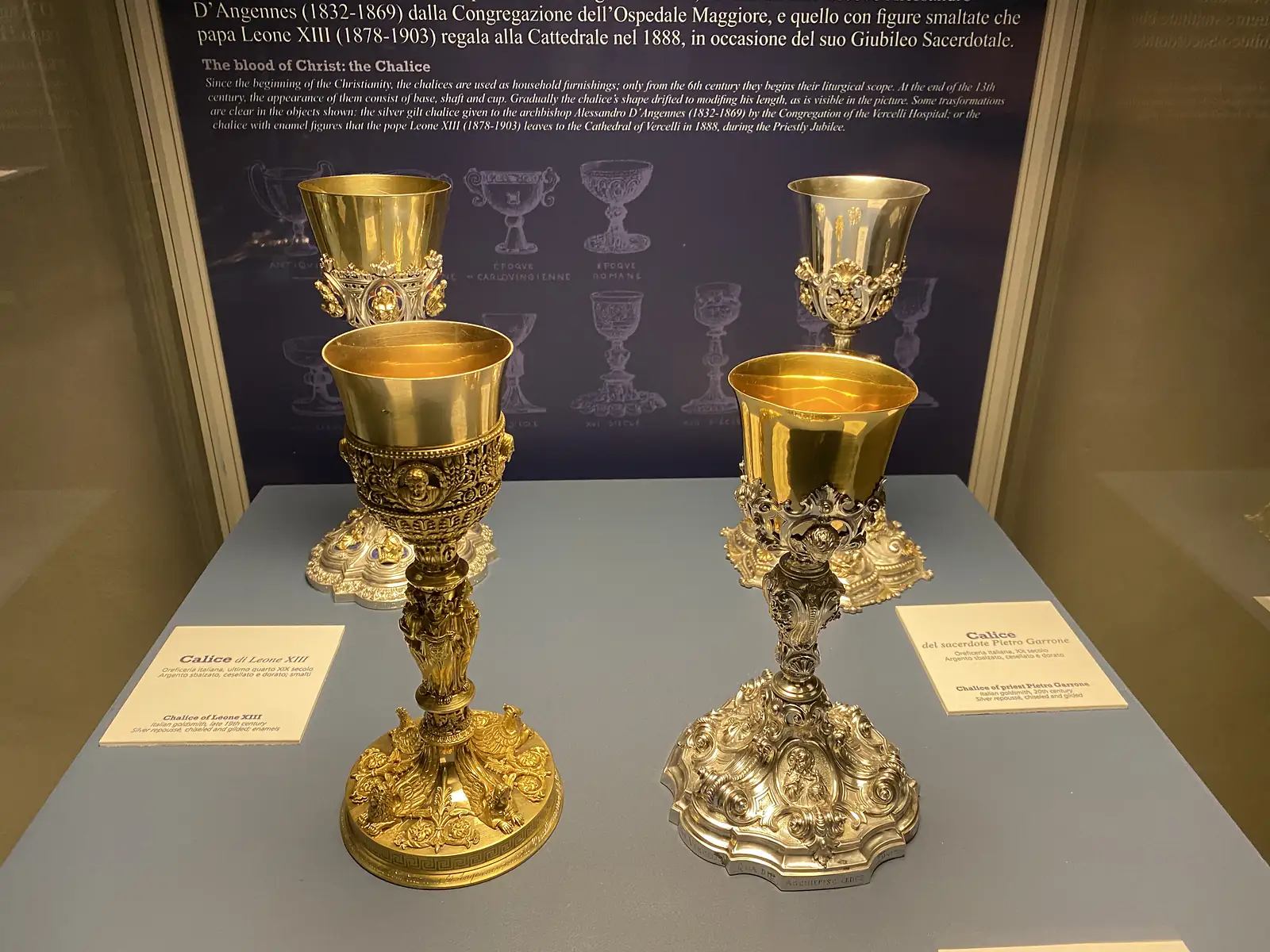 Two elaborate gilt and silver chalices on display at Vercelli Cathedral, labelled as the Chalice of Leo XIII and the chalice of the priest Pietro Garrone.