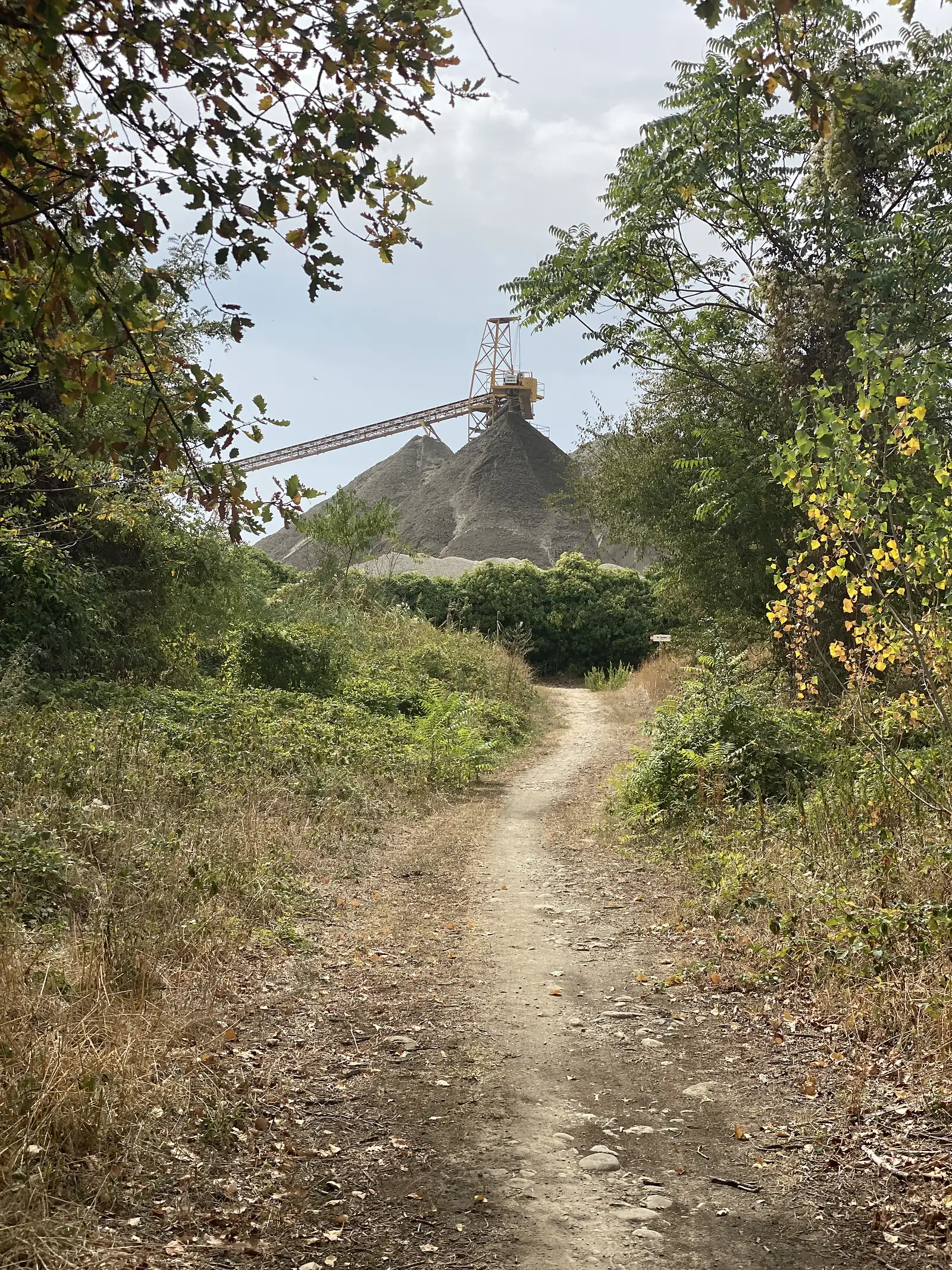 An industrial spill site rising above trees beside a moat, seen from a grassy path.