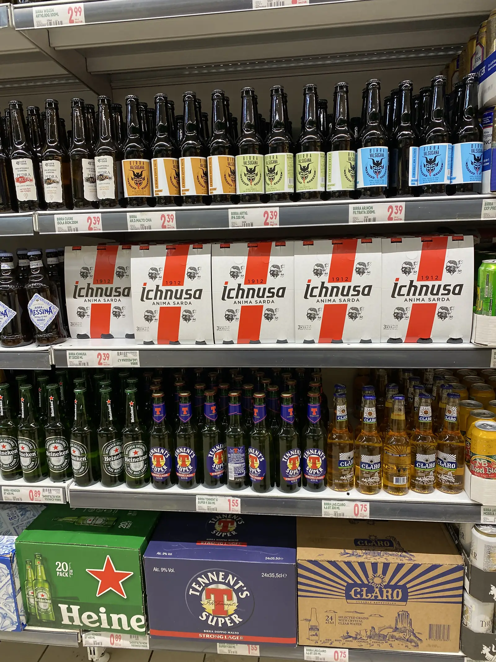 Supermarket shelves stacked with Italian beer, including boxed bottles of Ichnusa, Tennent's Super and Heineken, each with euro price tags.