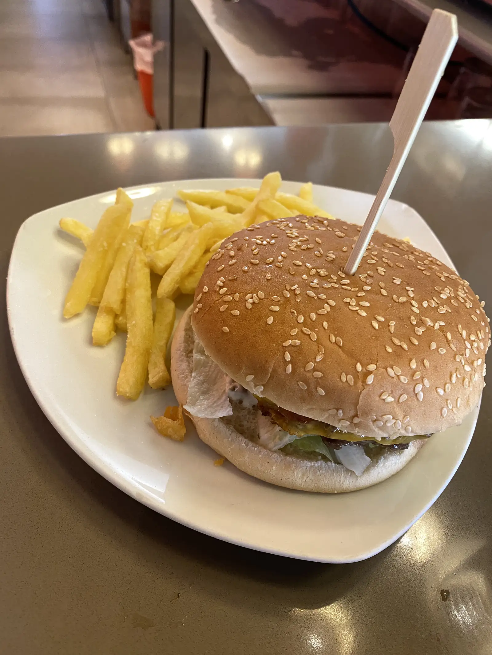 A burger in a sesame bun, skewered with a wooden pick, served with chips on a white plate on a bar counter.