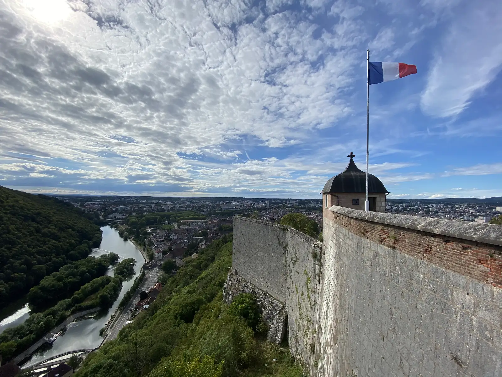 A French tricolour flies from a flagpole atop a domed stone sentry turret on the citadel wall, with the city spread out below.