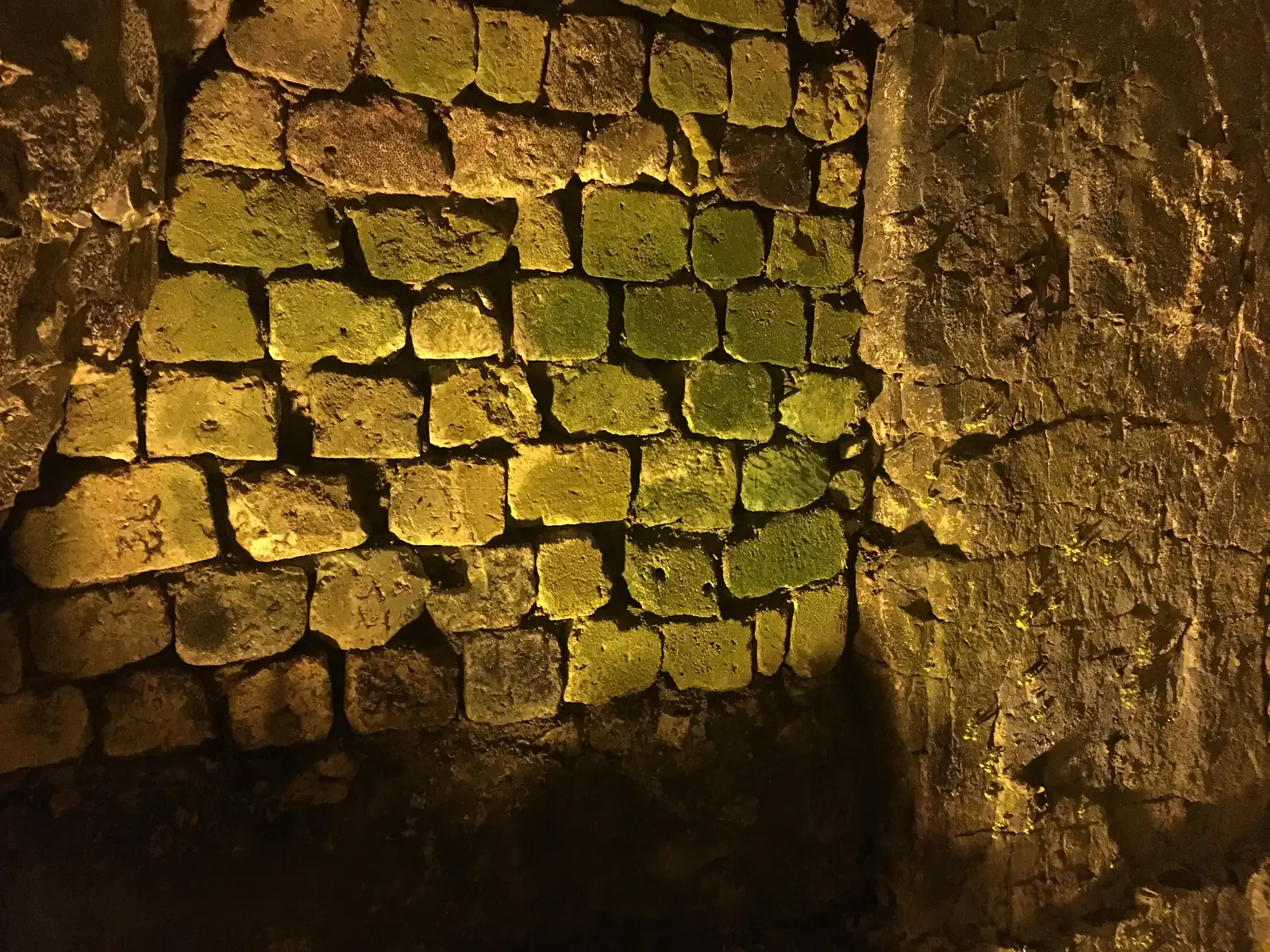 A vaulted underground passage cut through chalk bedrock, leading to a small brick-lined chamber, part of the wartime tunnels beneath Arras.