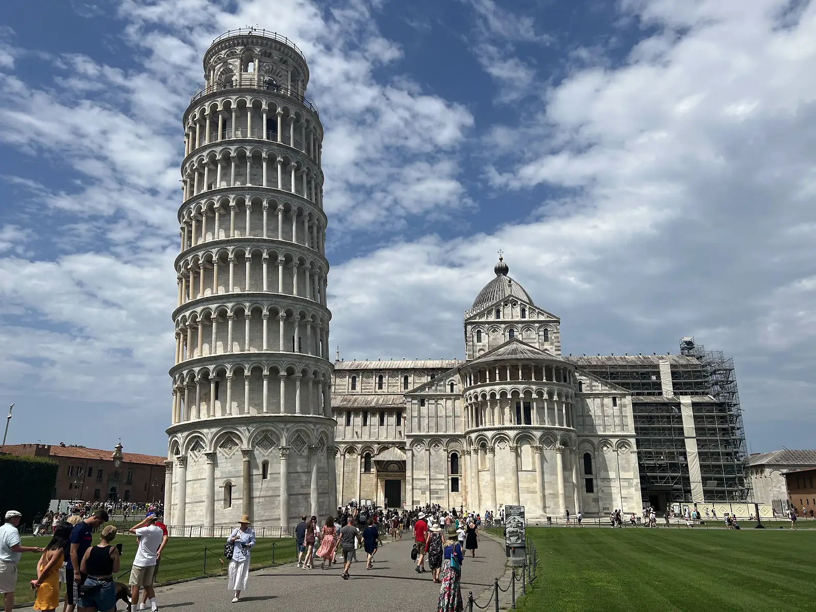 The Leaning Tower of Pisa and the cathedral behind it, with crowds of tourists on the piazza lawn in front.