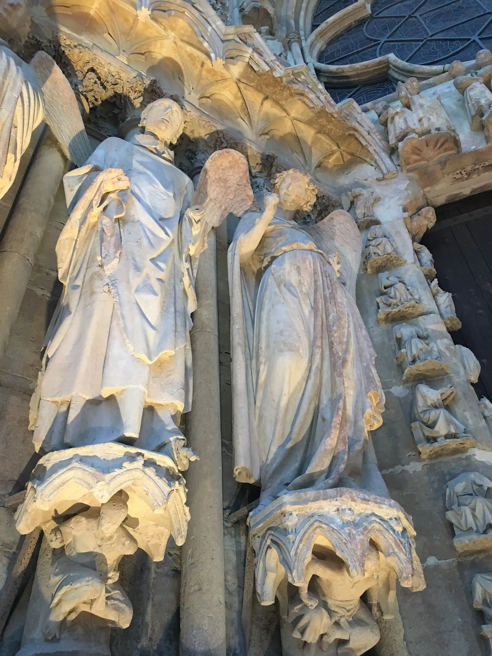 Close-up of weathered medieval stone statues on a cathedral portal, their carved robes and crowned heads worn smooth by centuries of erosion.