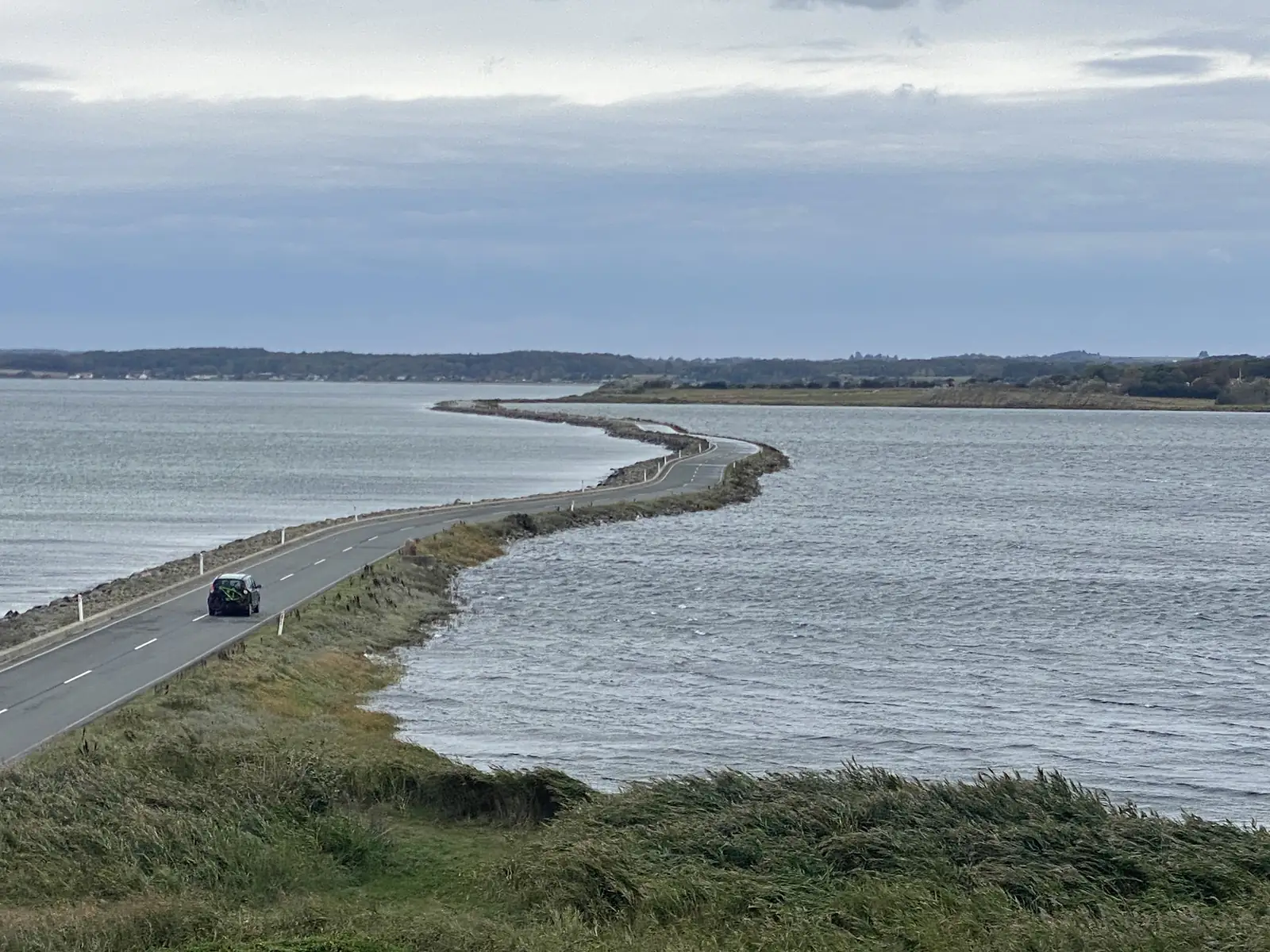 A narrow causeway road curving between two stretches of open water, with a single car crossing it.