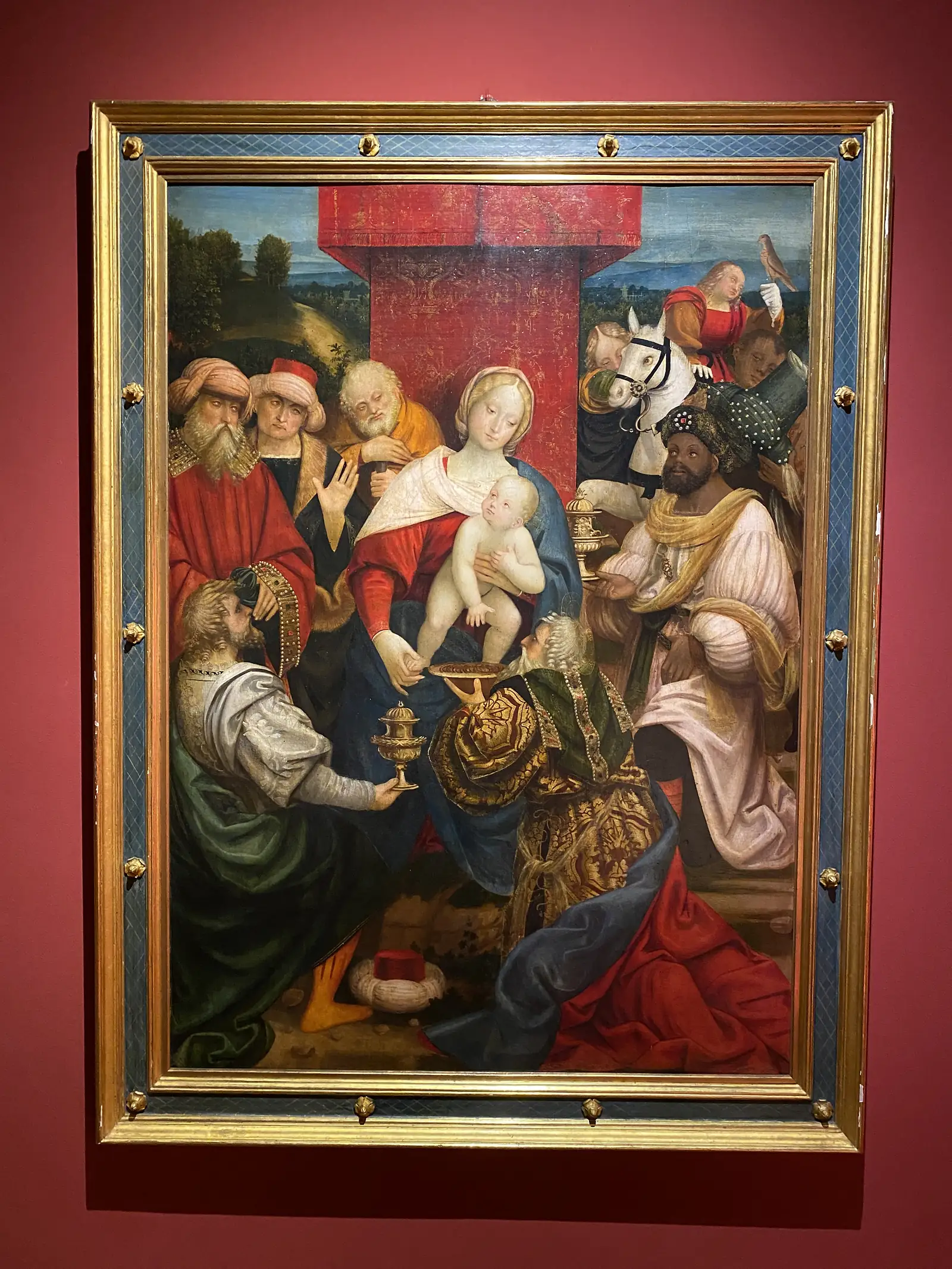 A Renaissance oil painting of the Adoration of the Magi in its gilt frame, showing the Virgin and Child receiving gifts from richly dressed kings and their retinue.