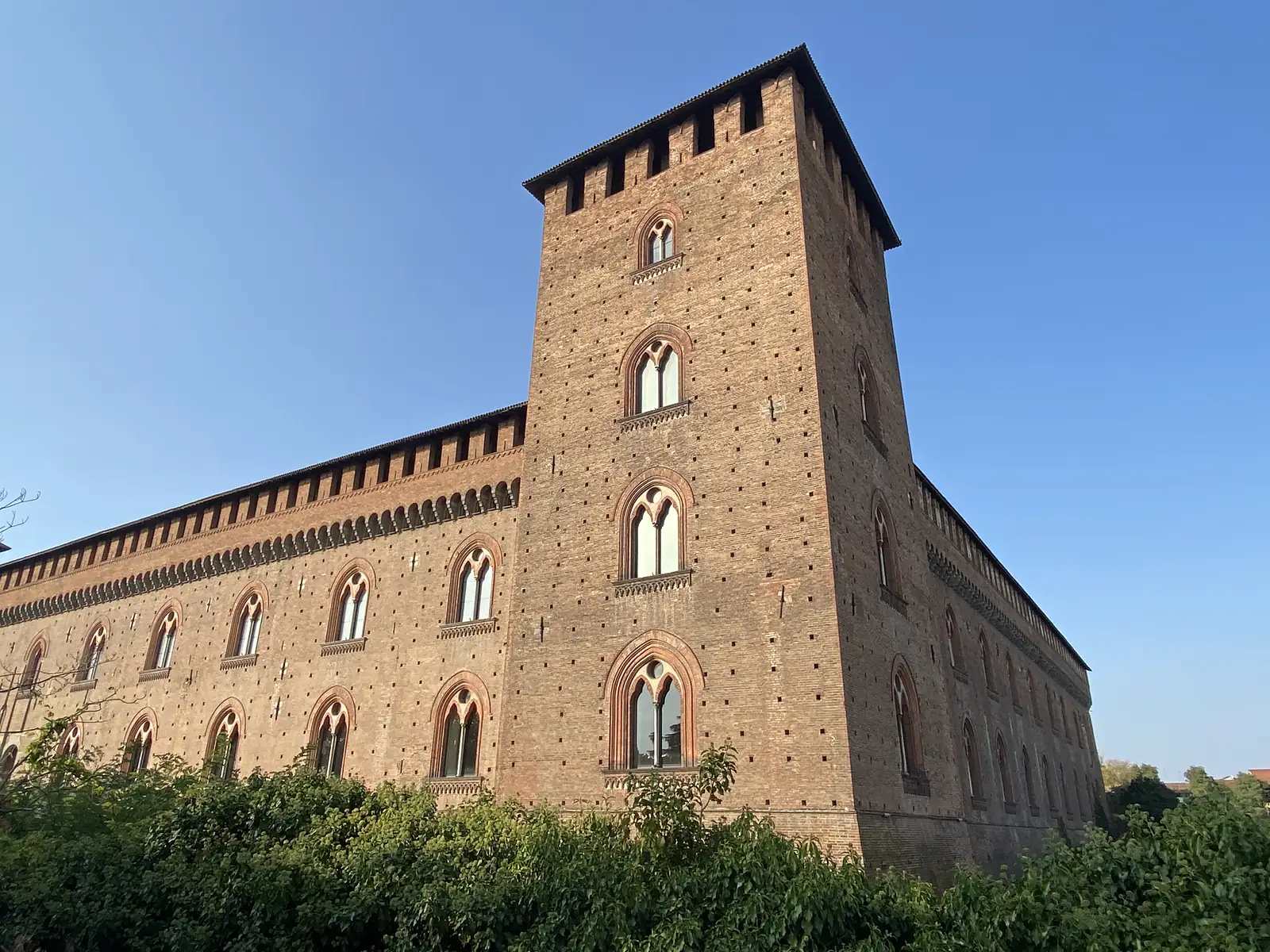A tall brick corner tower with crenellations and arched windows rises above the walls of a fortified medieval castle.