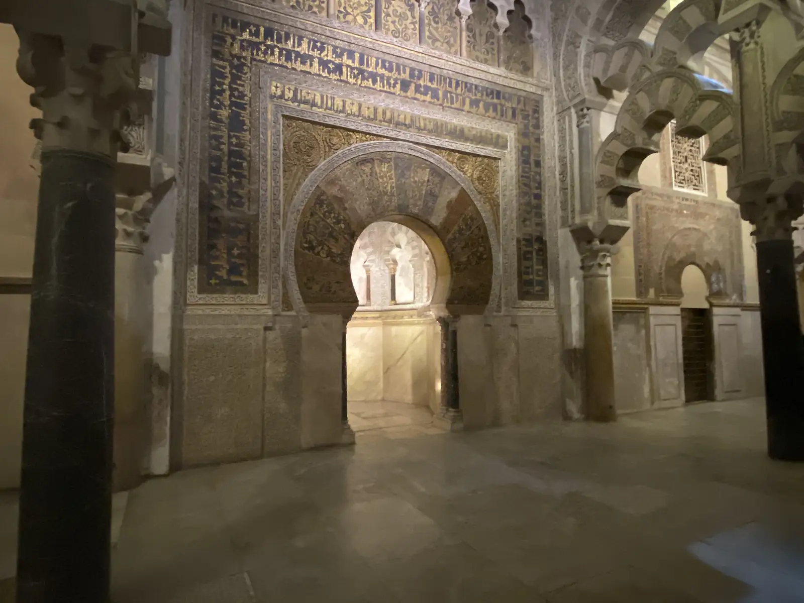 A richly gilded prayer niche, its horseshoe arch framed by gold mosaic and panels of blue-and-gold Arabic inscription.