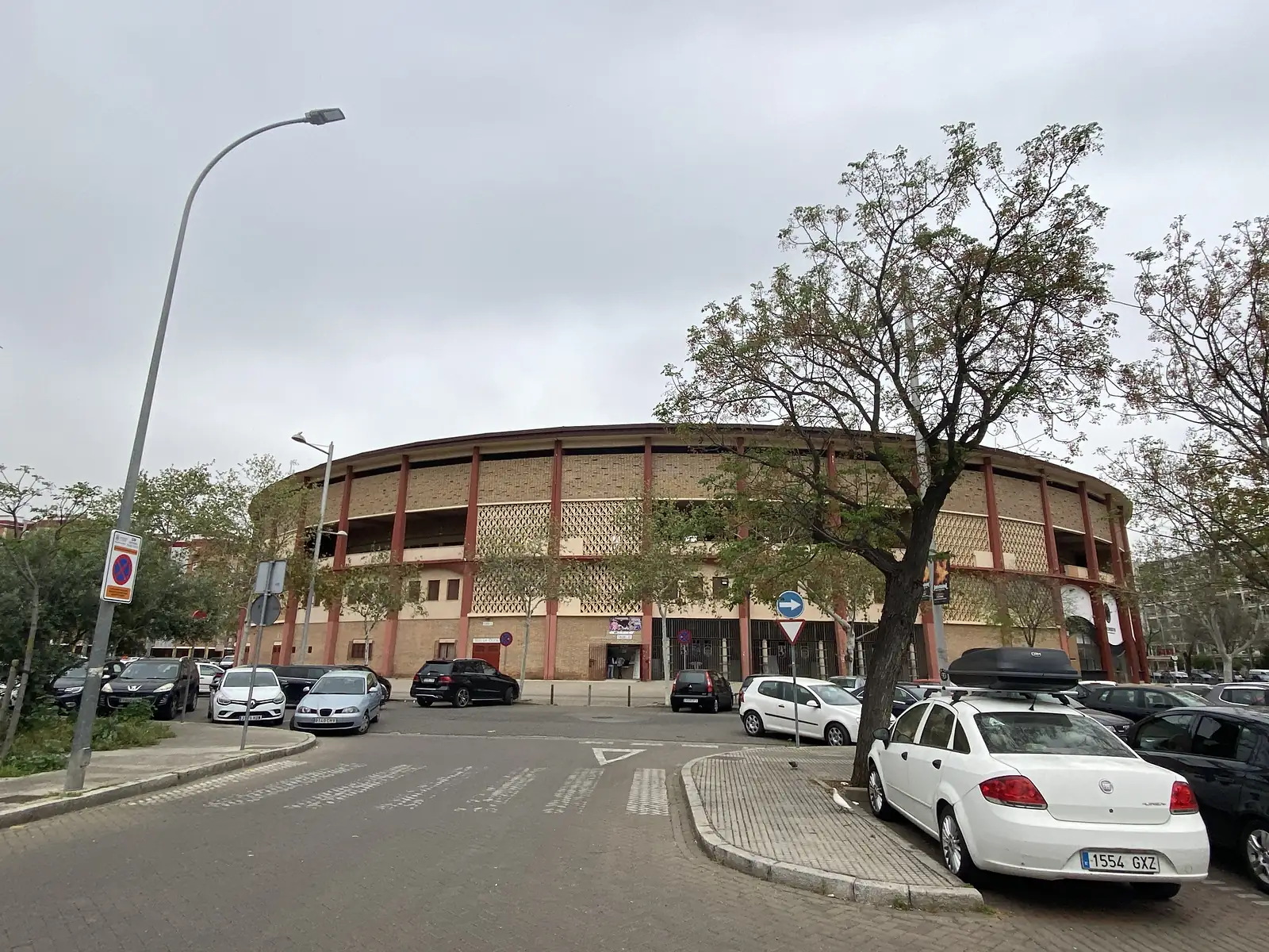 A large modern circular bullring of brick and pierced lattice walls between red pillars, cars parked all around it.