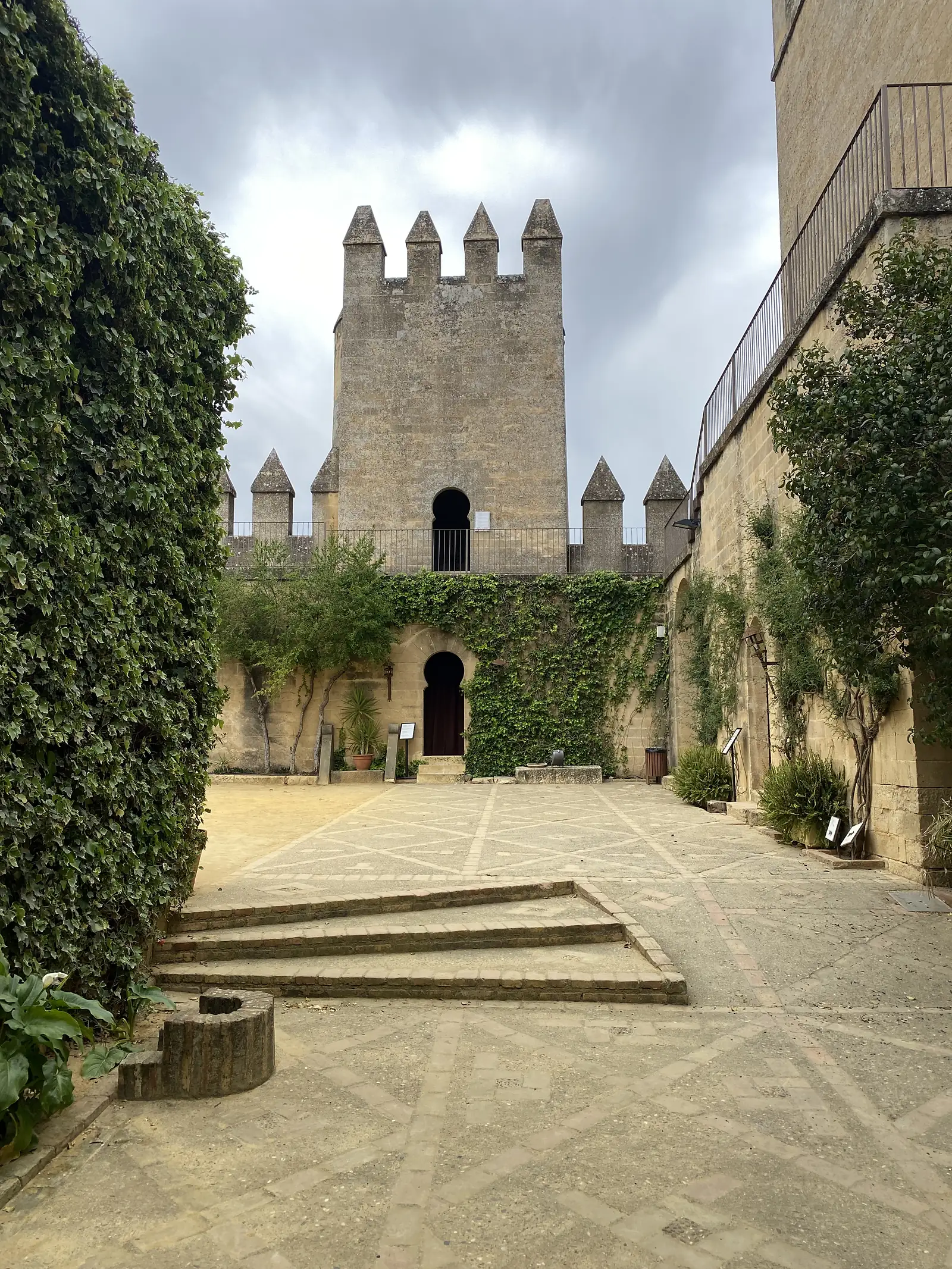 A castle courtyard with patterned stone paving and an ivy-covered wall, the battlemented keep rising above an arched doorway.