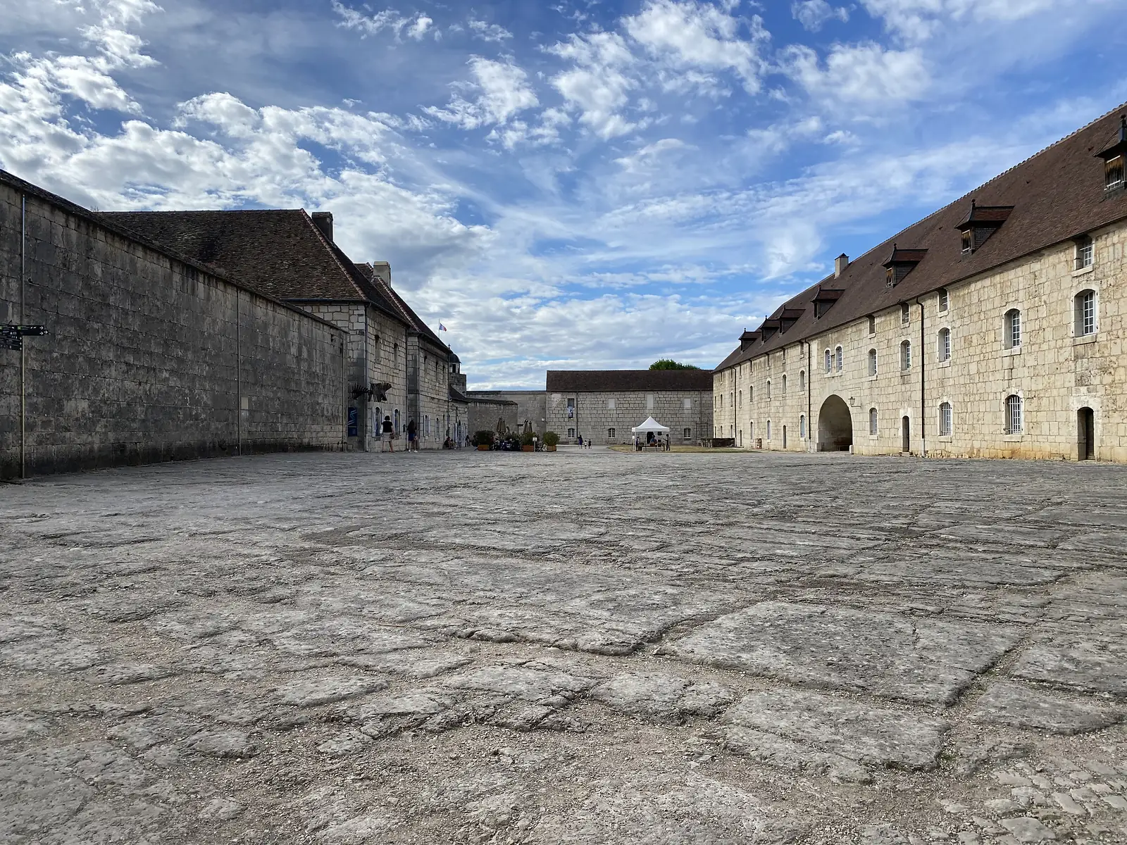 A wide stone courtyard is flanked by long, steep-roofed citadel buildings, with a marquee tent set up in the distance.