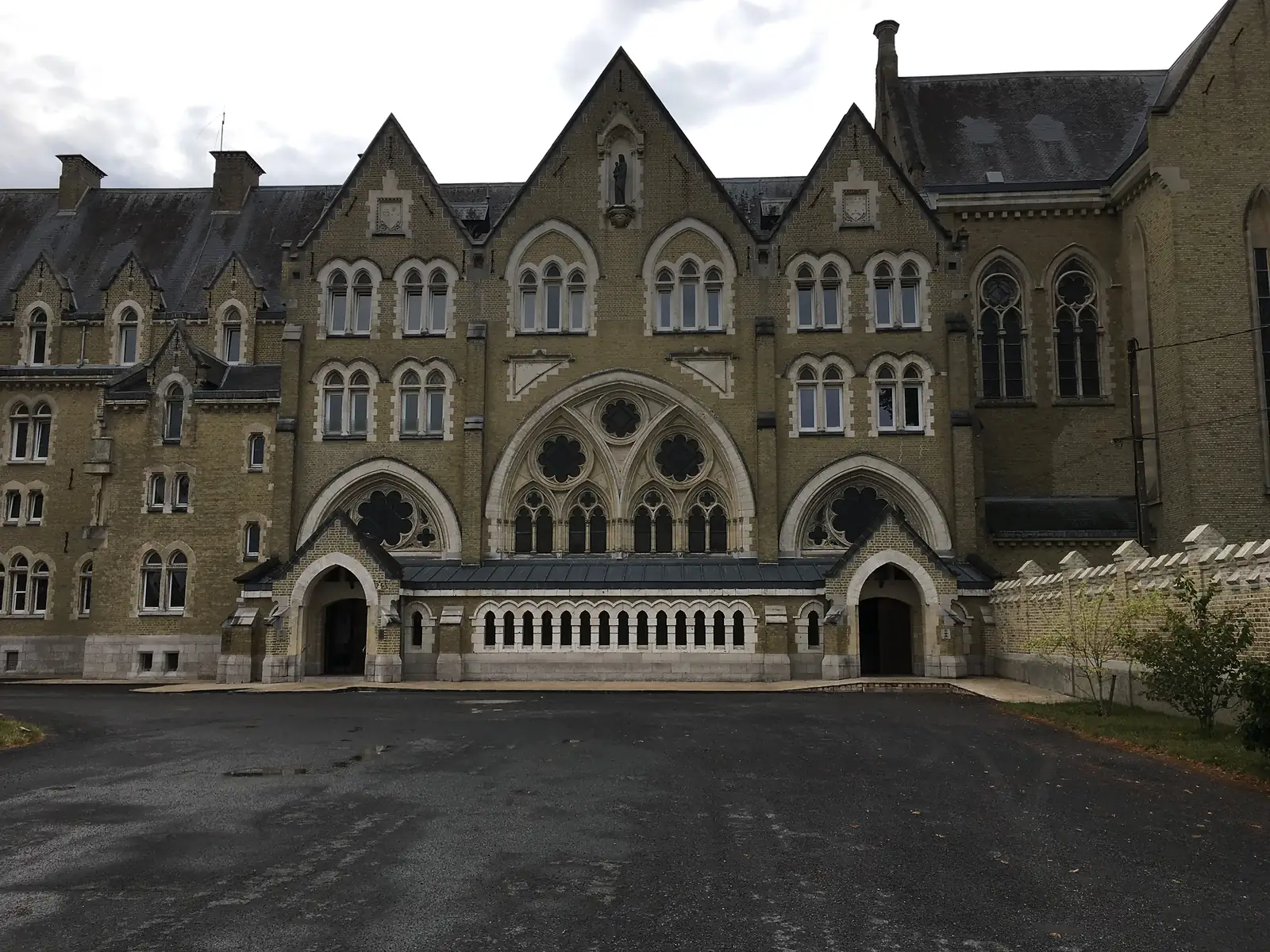 The elaborate Gothic-revival brick facade of a large religious or school building, with pointed arched windows, rose tracery and twin doorways opening onto an empty forecourt.