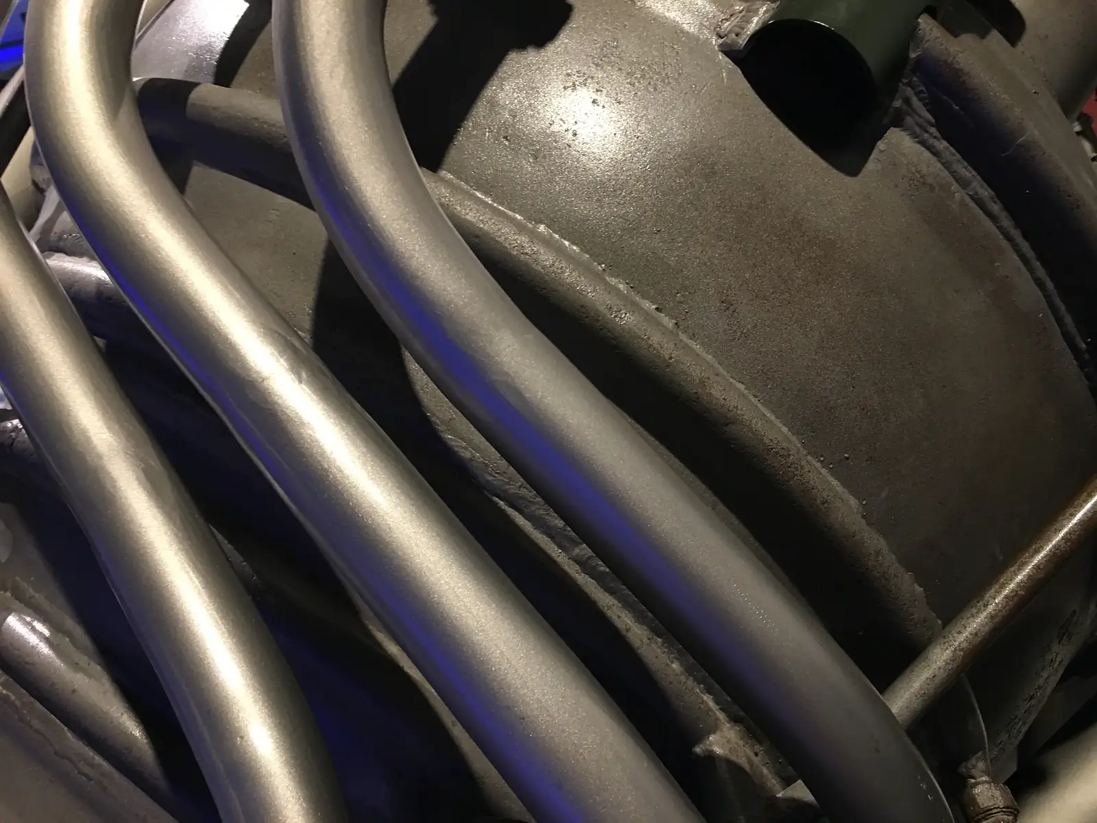 A close-up of thick grey pipework and cabling on a museum rocket exhibit, lit with a blue glow.