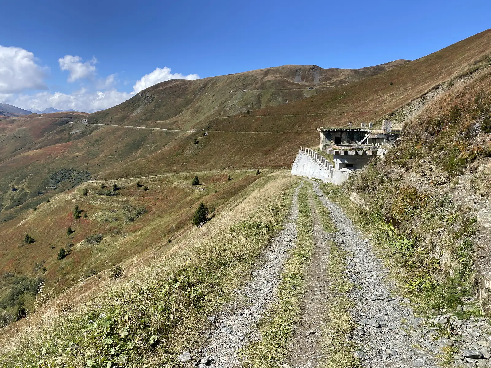 A grassy double-track climbs past a derelict concrete bunker cut into the hillside, with another track traversing the bare slopes opposite.