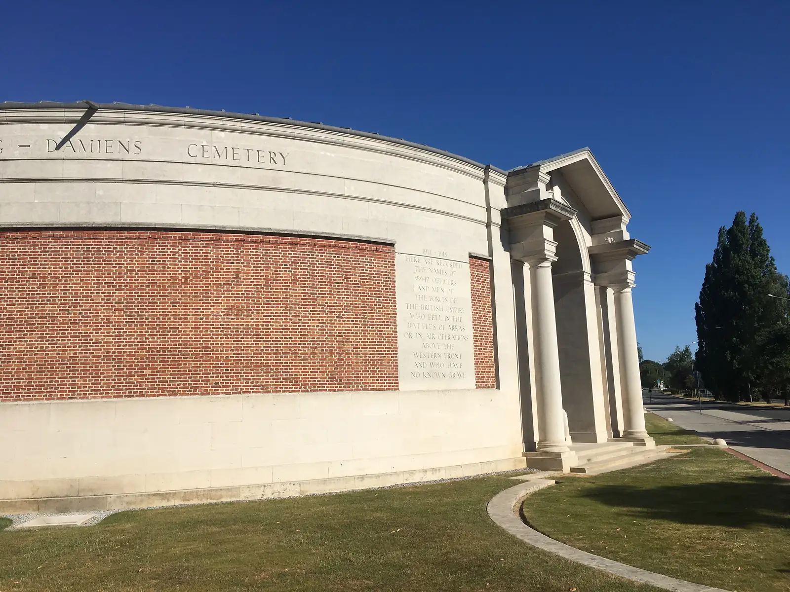 A cluster of red poppies wedged into the base of the Arras Memorial's stone panels, which are carved with long columns of soldiers' names.
