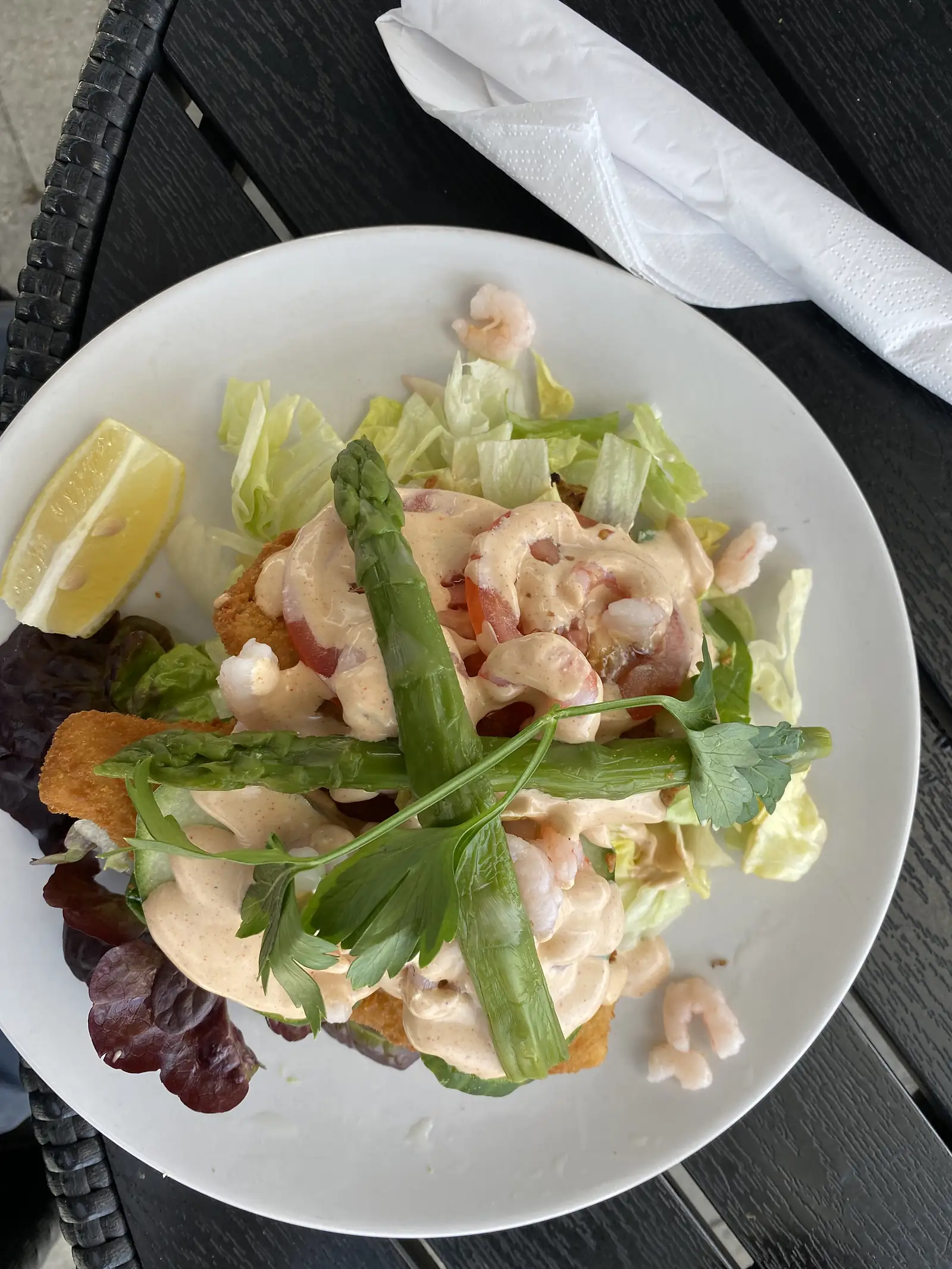 A plate of breaded fried fish topped with prawns in pink dressing, asparagus and shredded lettuce, with a lemon wedge.