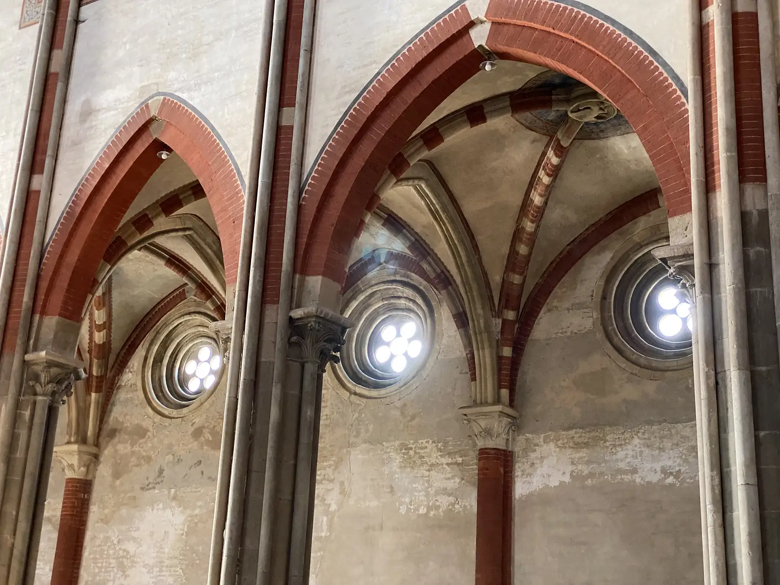 Gothic ribbed arches and rose windows in the basilica's aisle, the red-and-cream brickwork catching light from the round openings.