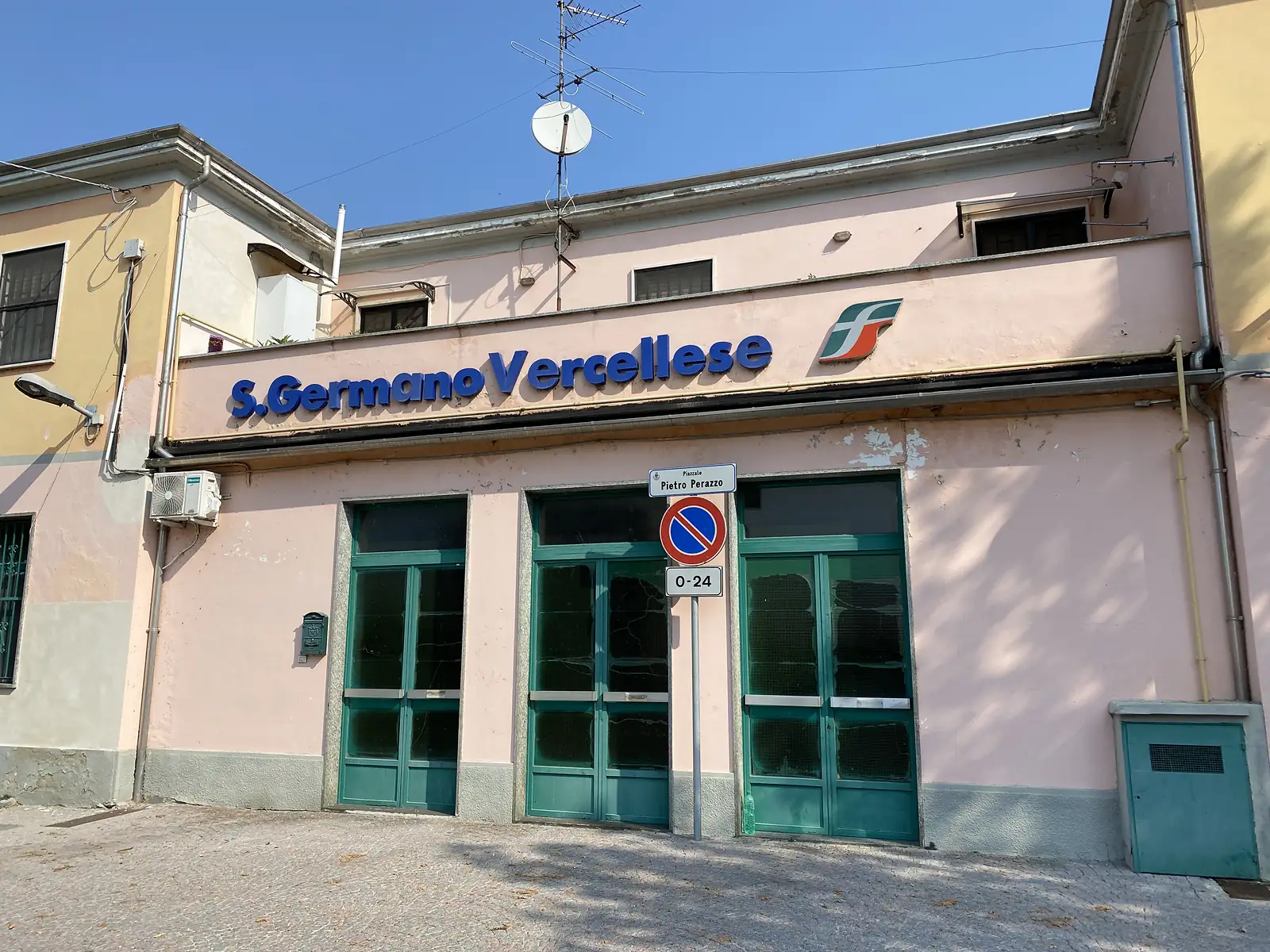 The pink station building of S. Germano Vercellese, its facade lettered with the town name and the Trenitalia logo above green shuttered doors.