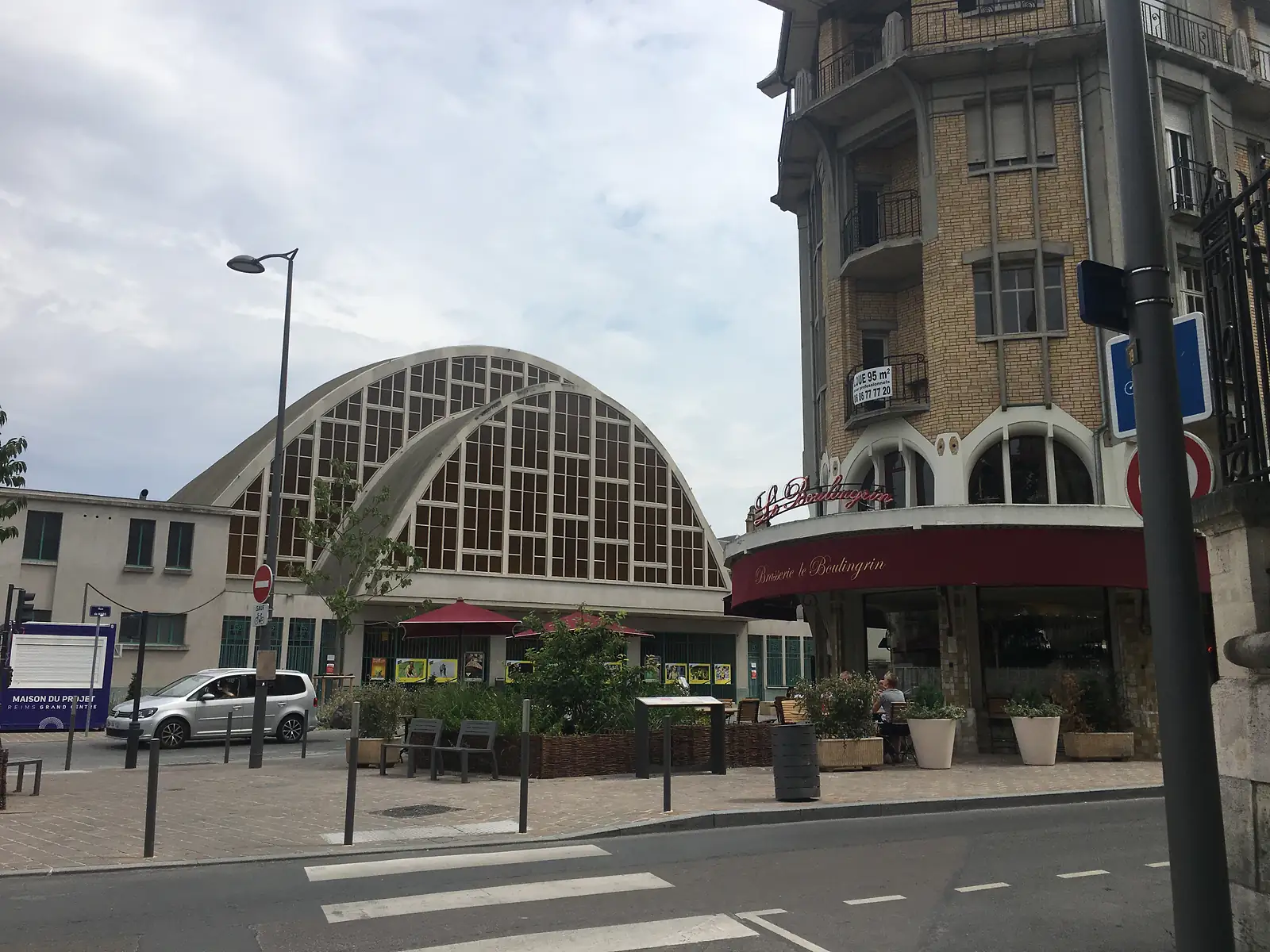 The arched glass roof of the Boulingrin market hall in Reims rises behind the neon-lit sign of Brasserie le Boulingrin and its red awning.