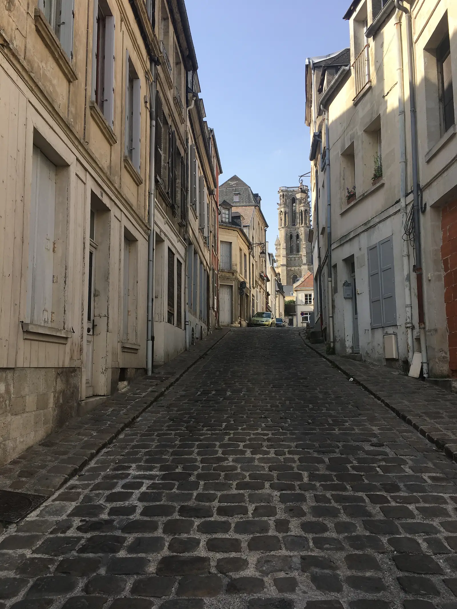 A narrow street of pale stone buildings leads towards the distant towers of the cathedral, visible above the rooftops ahead.