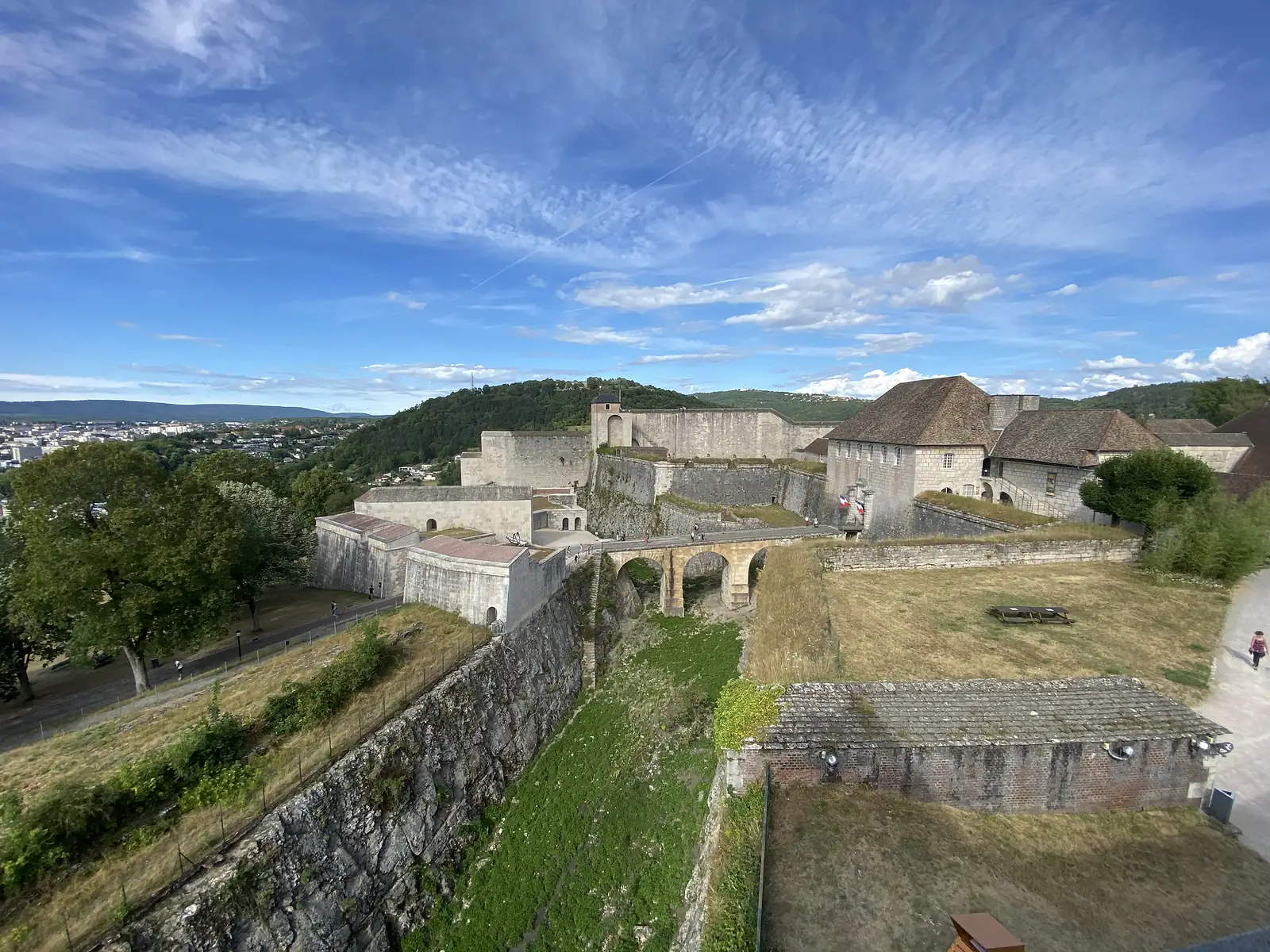 The star-shaped stone ramparts of a hilltop citadel, linked by an arched bridge, overlook wooded hills and a grassy picnic area.