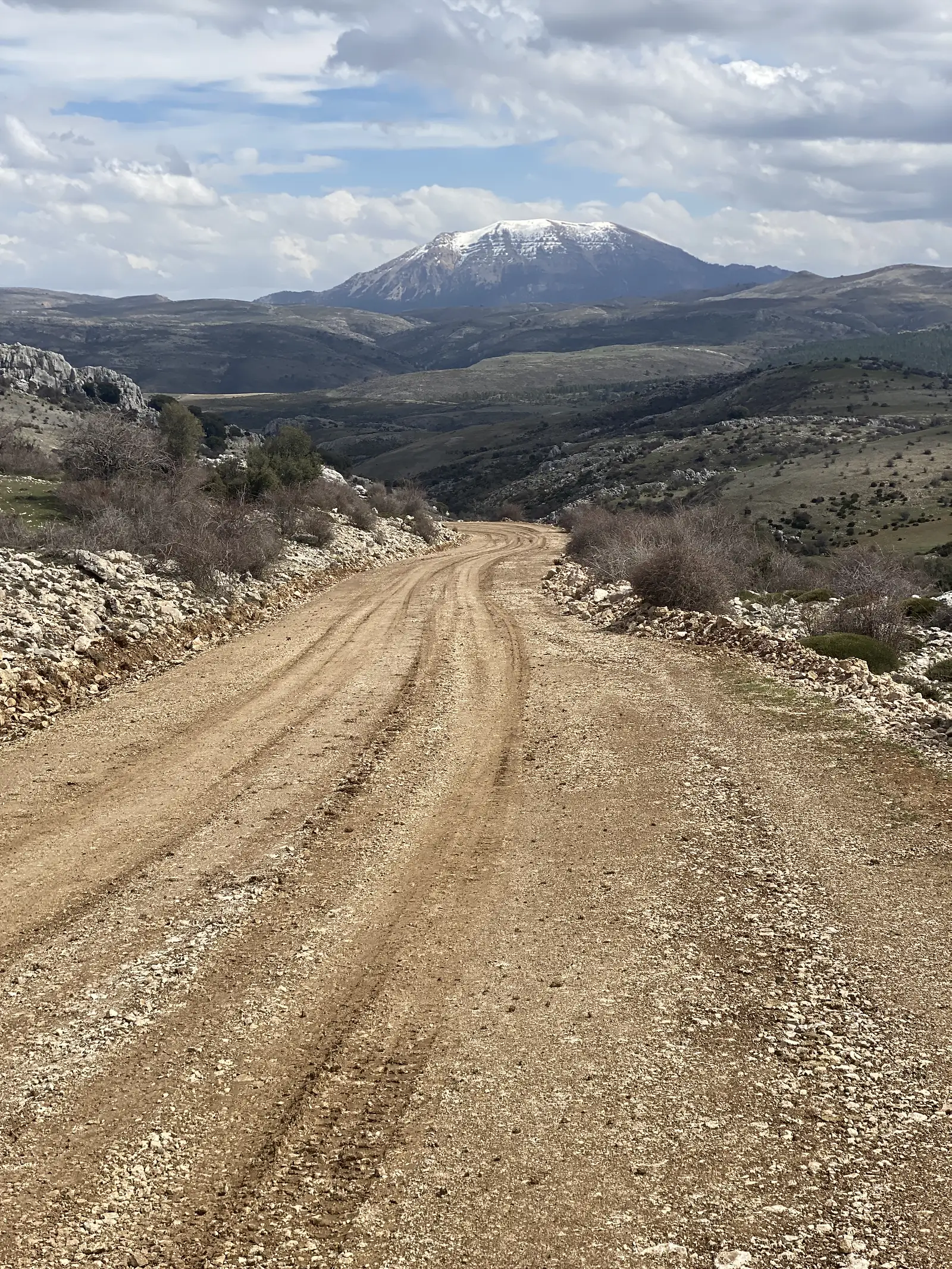 A wide dirt track dropping away towards a snow-capped conical mountain rising beyond rolling limestone country.