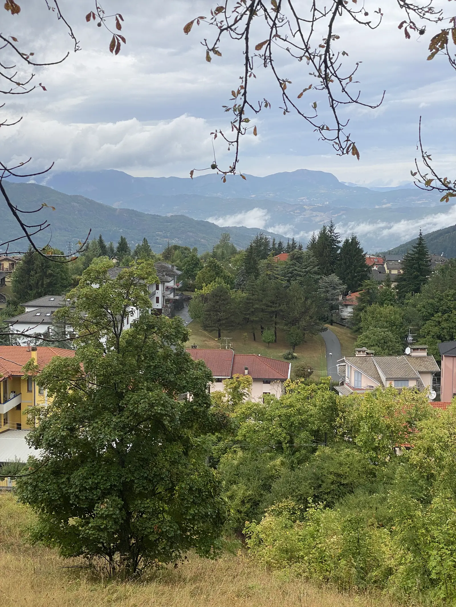 Red-tiled rooftops of a hillside village nestle among trees, with layered mountain ridges receding beneath a partly clouded sky.