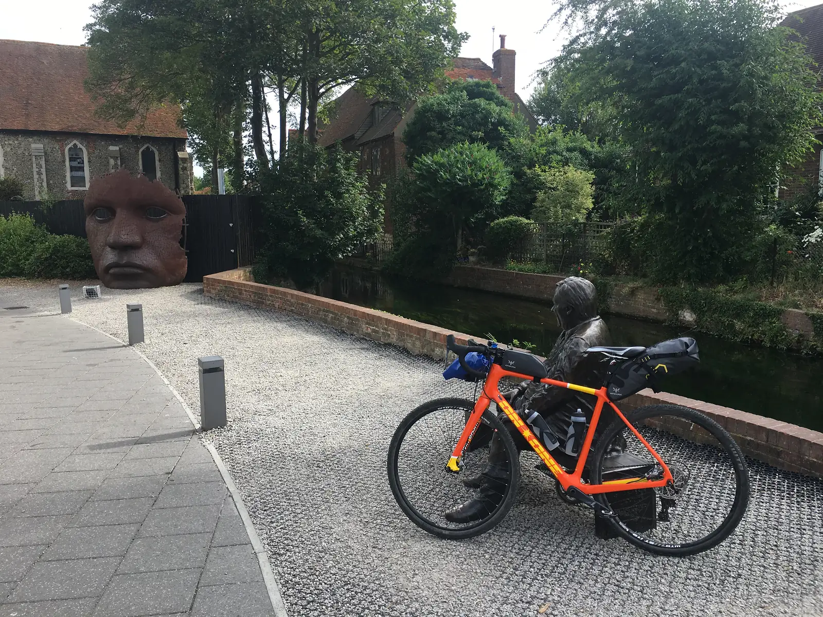 Orange bike leaning on a bronze statue of some geezer
