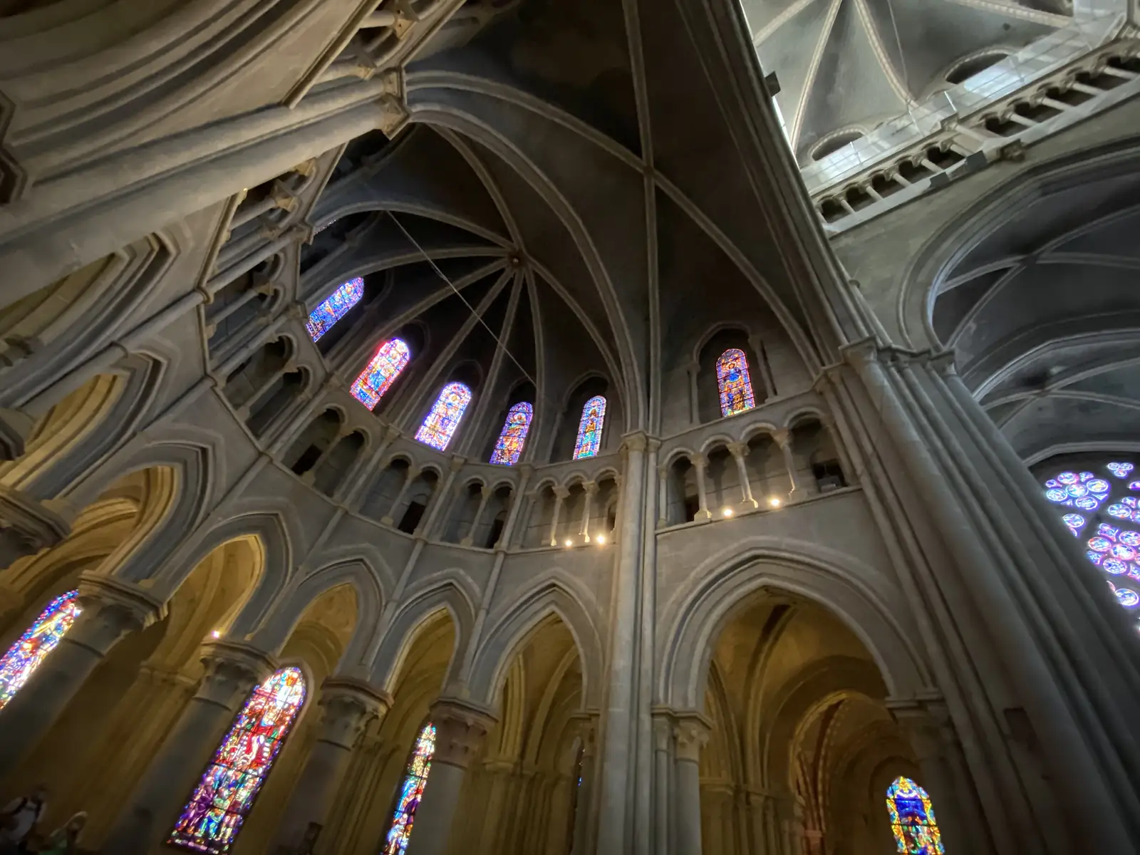 Looking up inside Lausanne Cathedral at the ribbed stone vaulting of the apse, ringed with tall stained-glass windows.