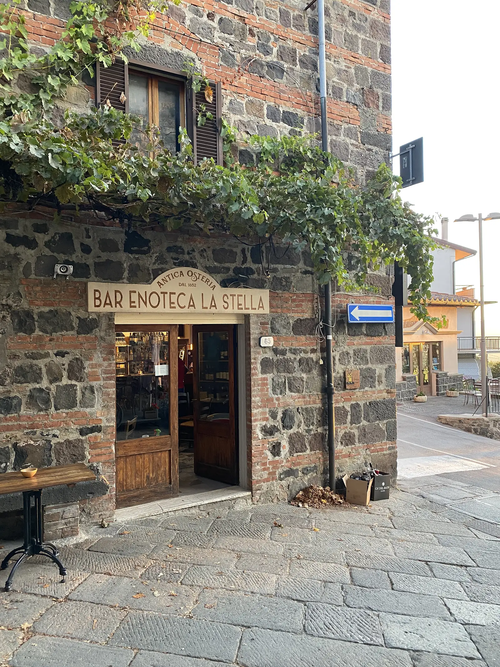 The stone façade of Bar Enoteca La Stella, Antica Osteria dal 1852, on a cobbled Italian street, with a grapevine trailing across the wall above the doorway.
