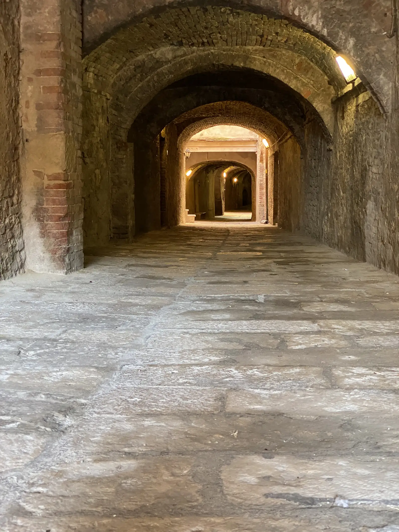 A view straight down through the stacked brick-vaulted floors of a medieval tower, each level lit by a small lamp.