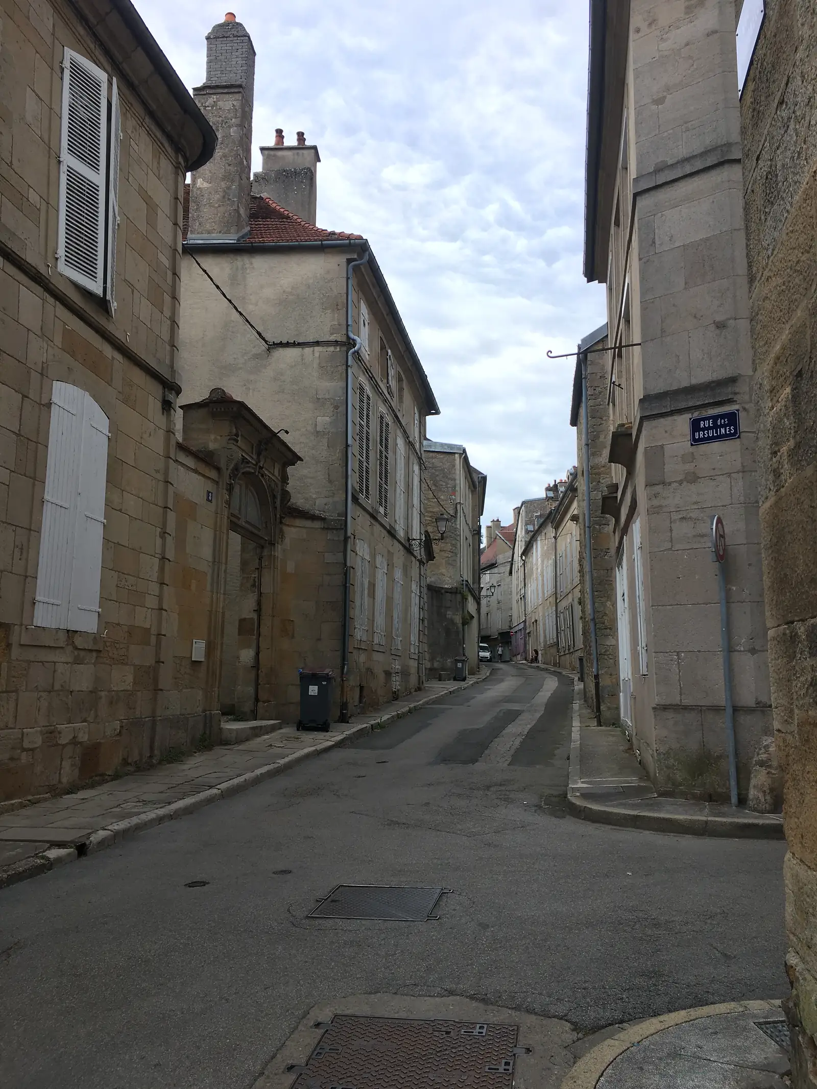 A narrow street in Langres lined with tall stone houses and shuttered windows, with a blue street sign reading Rue des Ursulines.