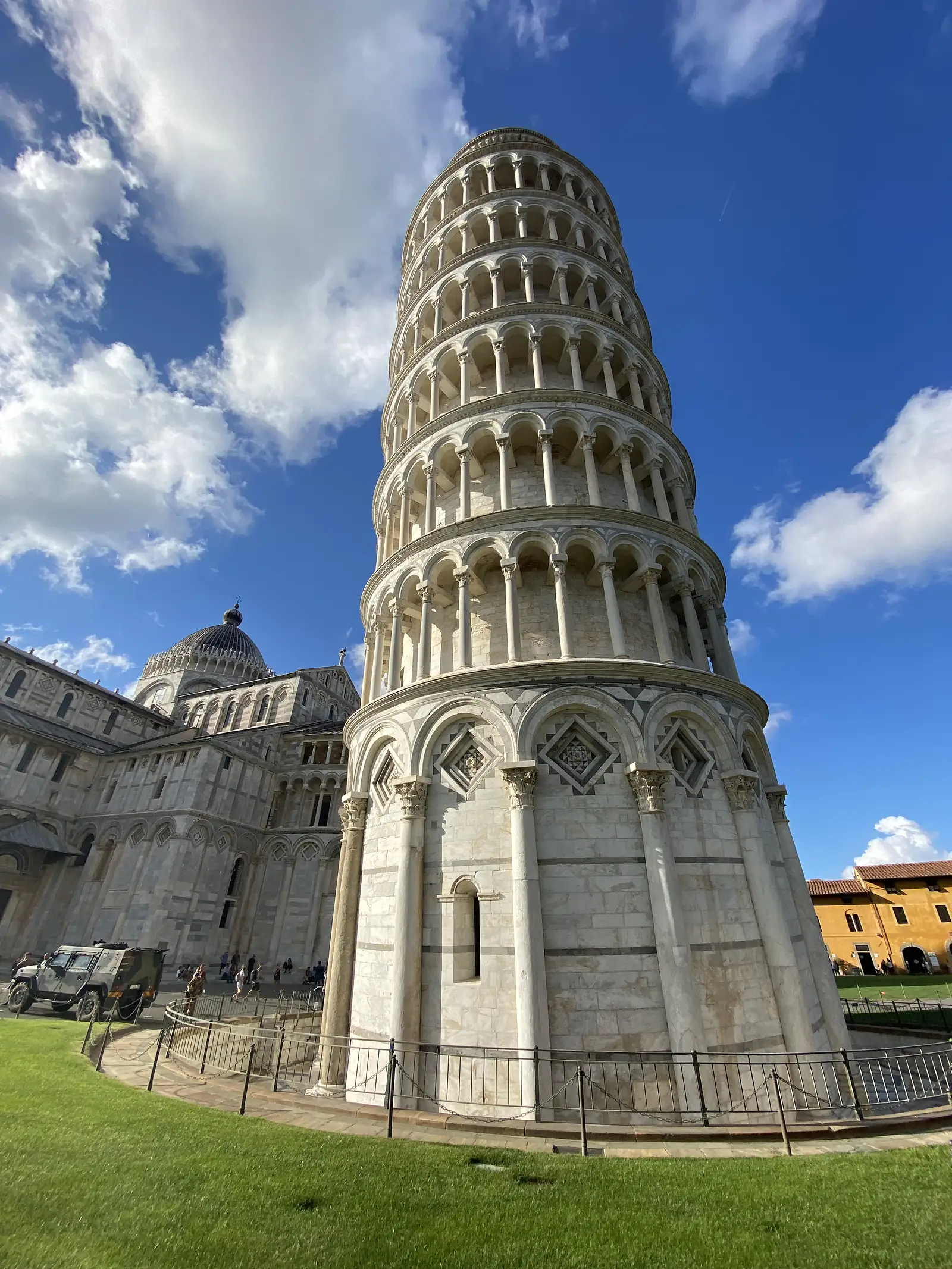 The Leaning Tower of Pisa seen from below, its rows of marble columns curving away at a steep tilt beside the cathedral's dome.