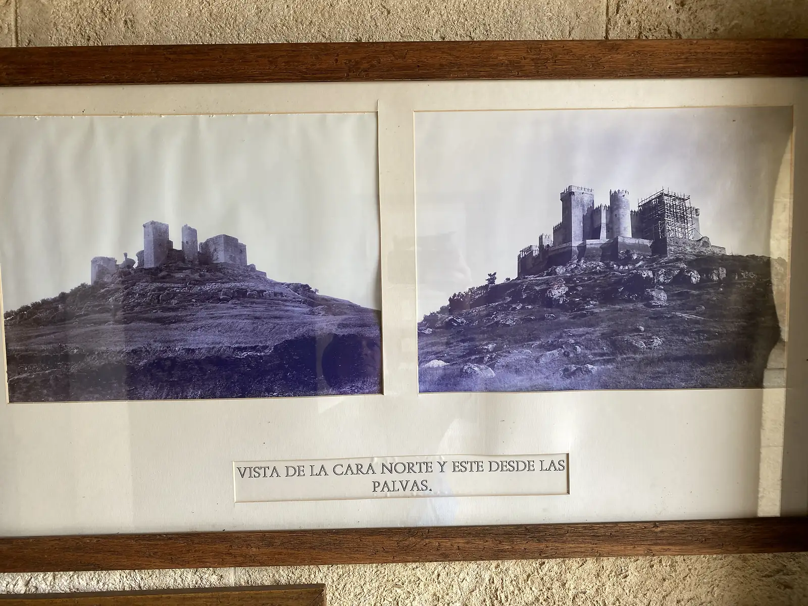 A framed pair of old black-and-white photographs showing the castle before and during restoration, captioned "VISTA DE LA CARA NORTE Y ESTE DESDE LAS PALVAS".
