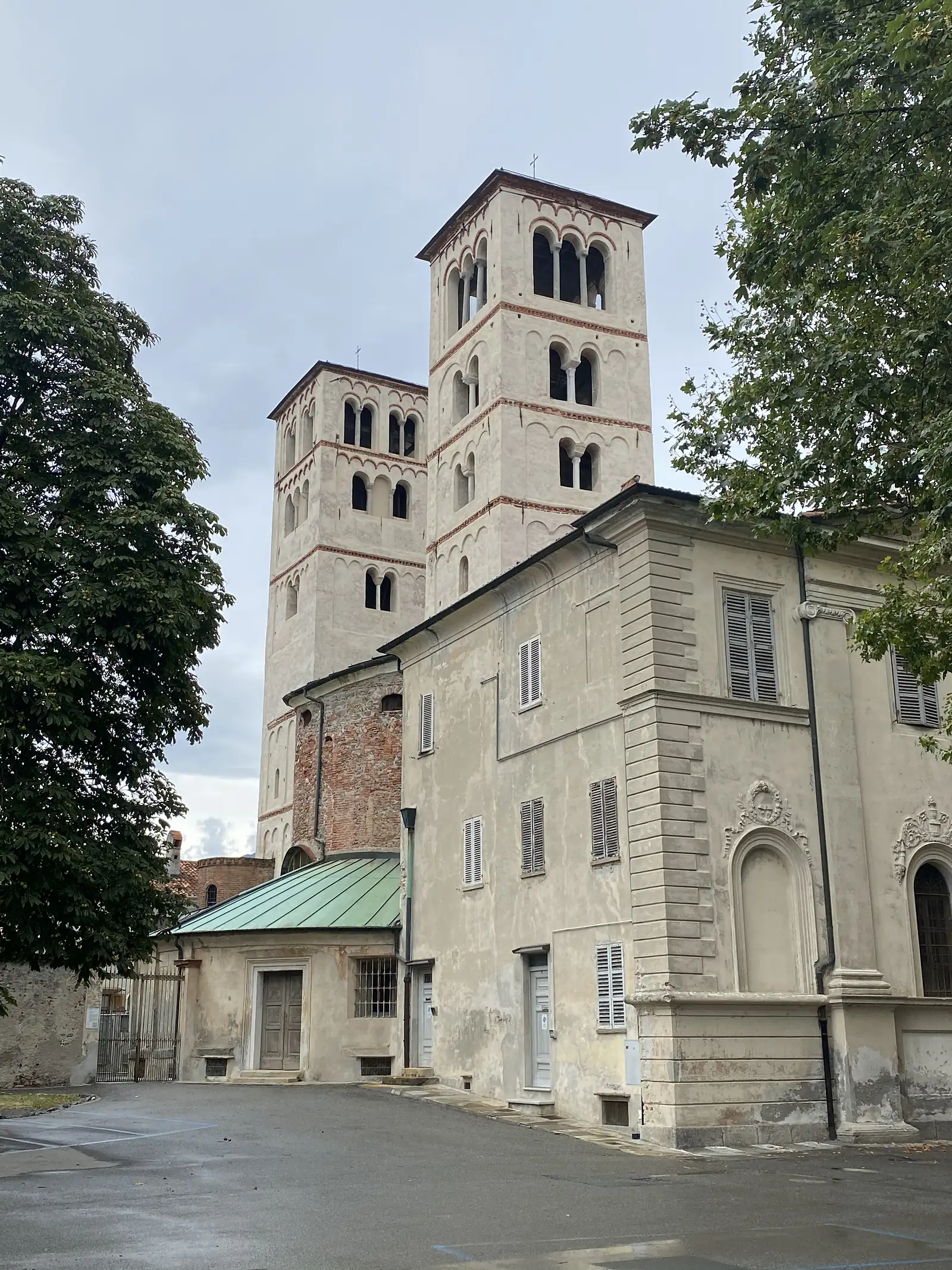 Two tall Romanesque bell towers with tiered arched windows and terracotta banding rise above the apse of Ivrea Cathedral, framed by chestnut trees.
