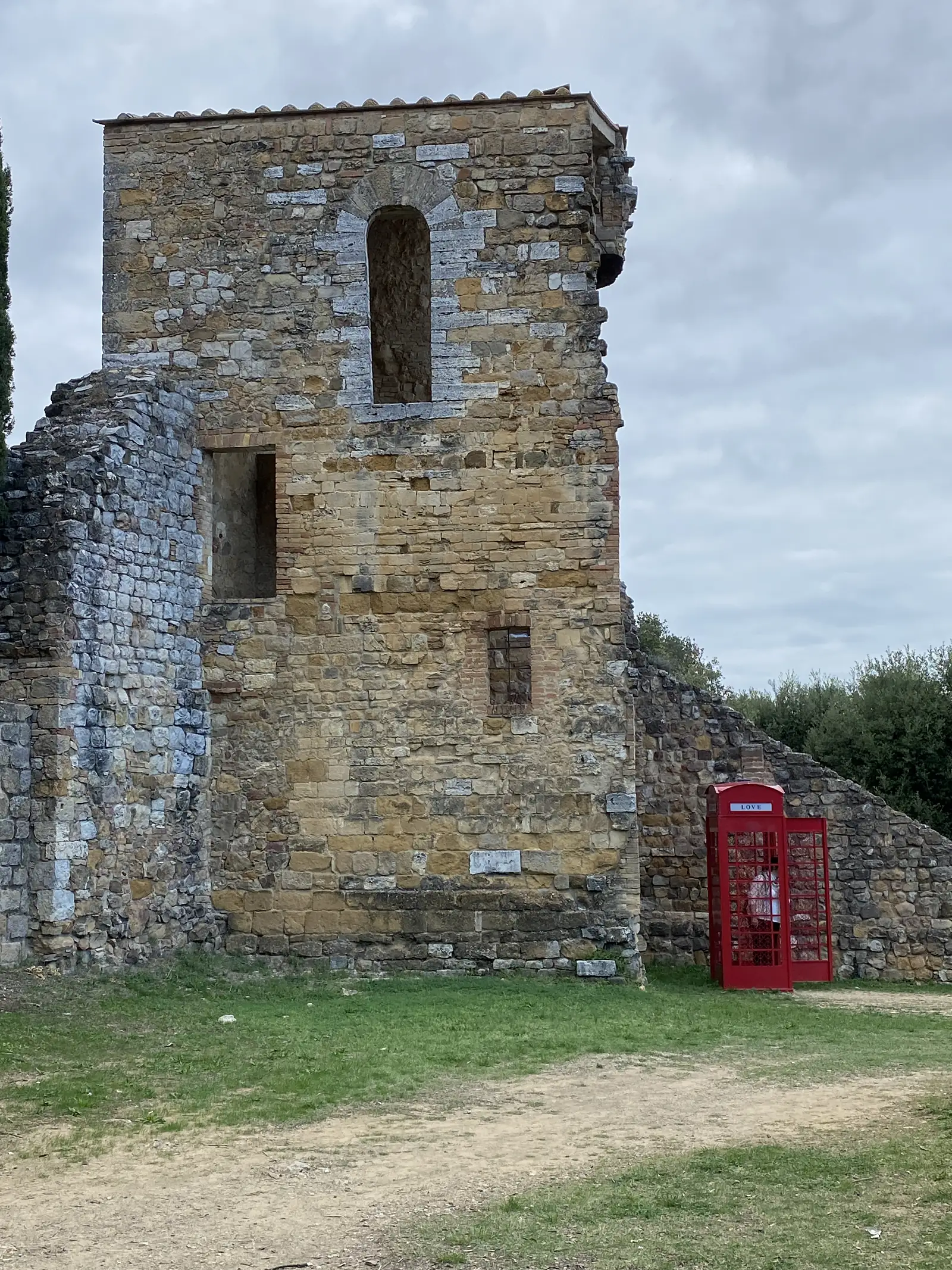 A ruined stone tower on open grassland, with an incongruous red telephone box marked LOVE standing beside its wall.