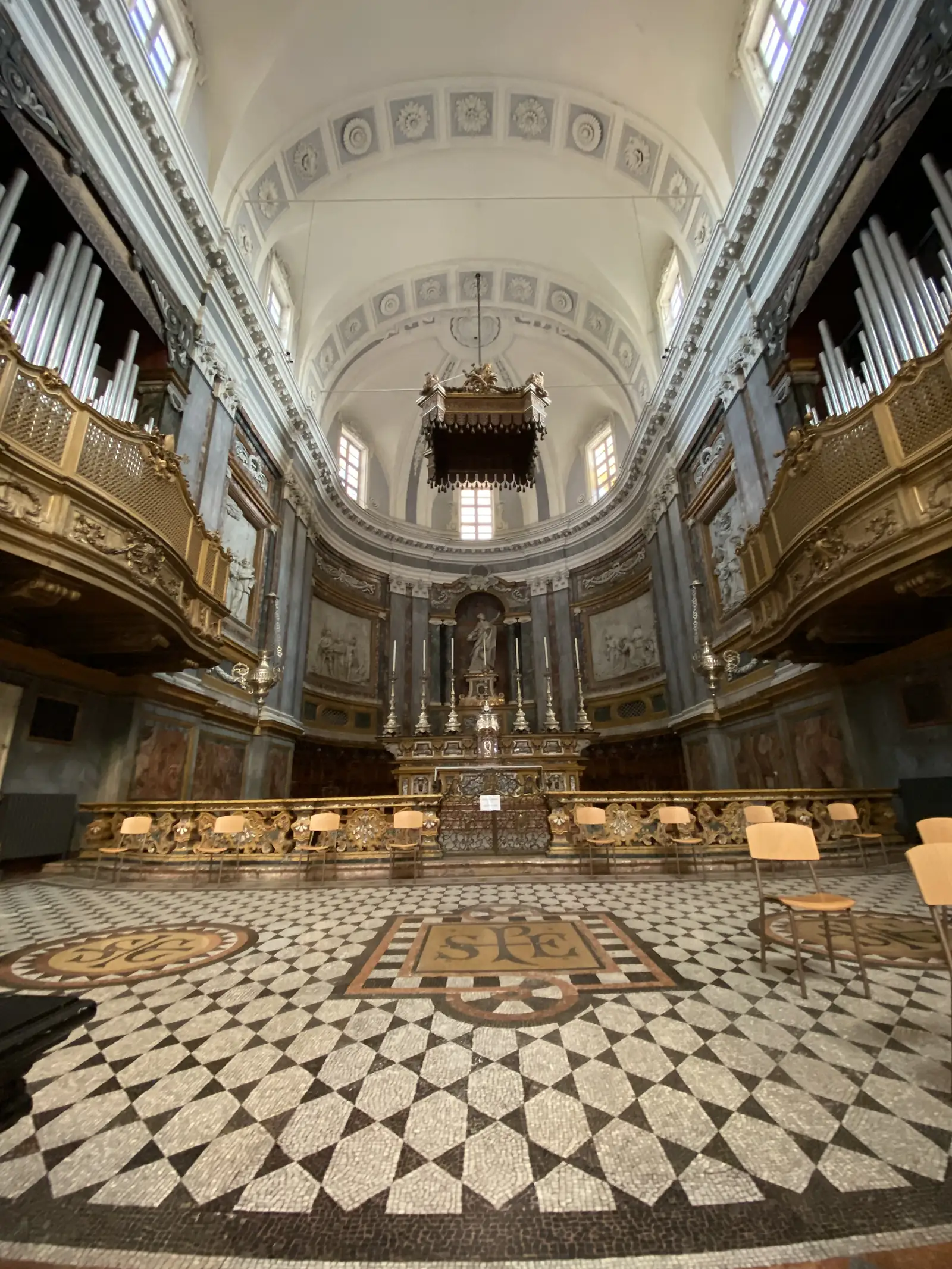 Looking down the nave towards the organ loft, past tiled arches and a black-and-white marble floor inlaid with the monogram 'IHS'.
