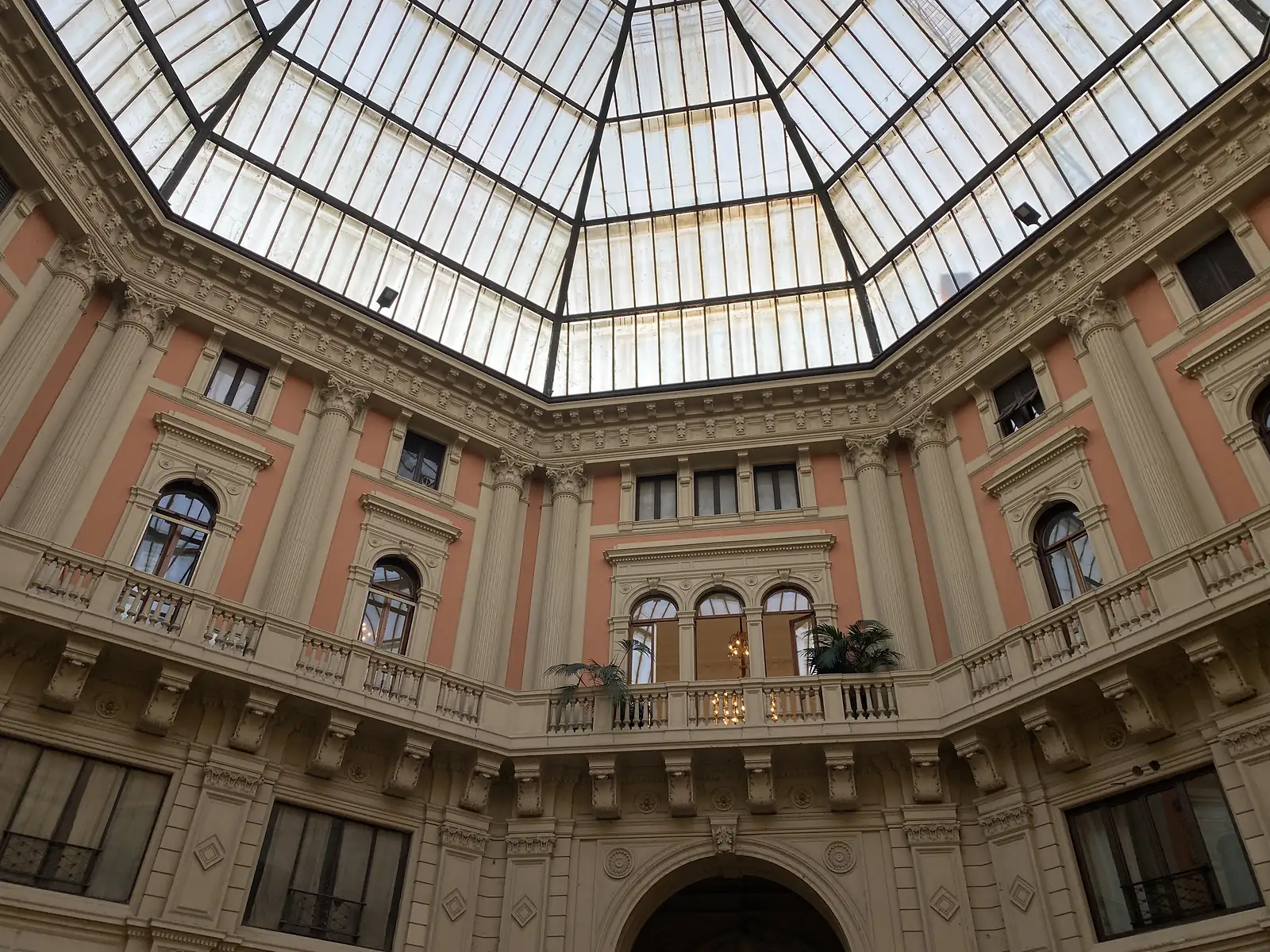 A glazed octagonal skylight crowns a grand courtyard, its peach-and-cream walls lined with balustraded balconies and Corinthian pilasters.