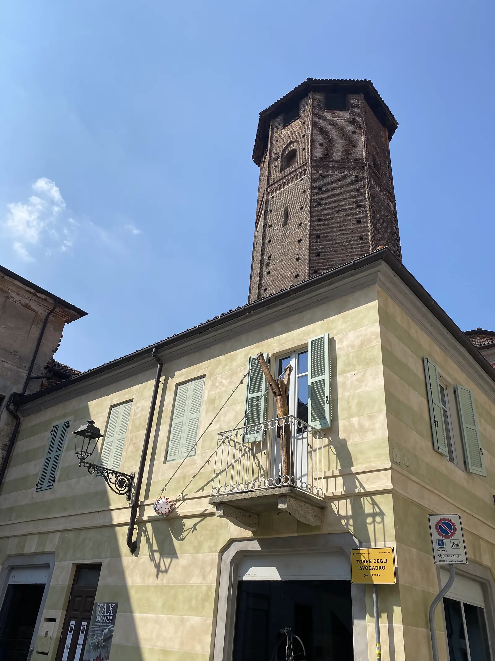 Looking up at the medieval brick Torre degli Avogadro rising above a row of shuttered townhouses, its identifying plaque fixed to the wall below.