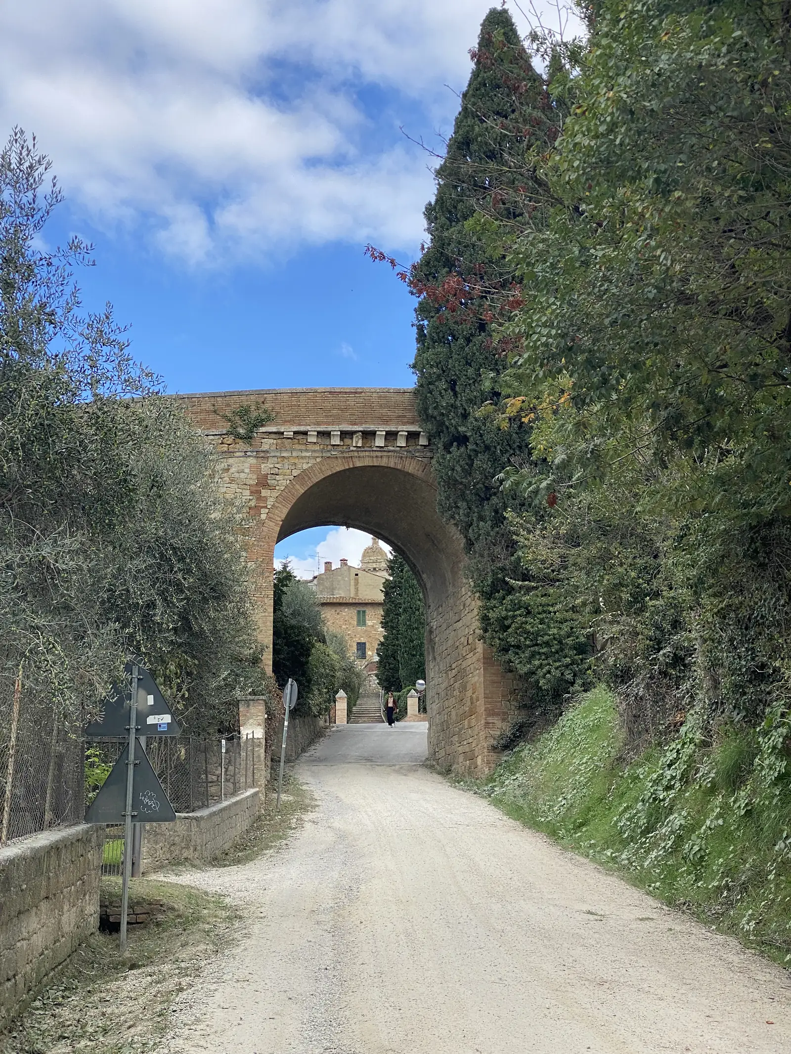 A brick archway set into a stone town wall, framing a paved lane leading past shuttered buildings into the historic centre.
