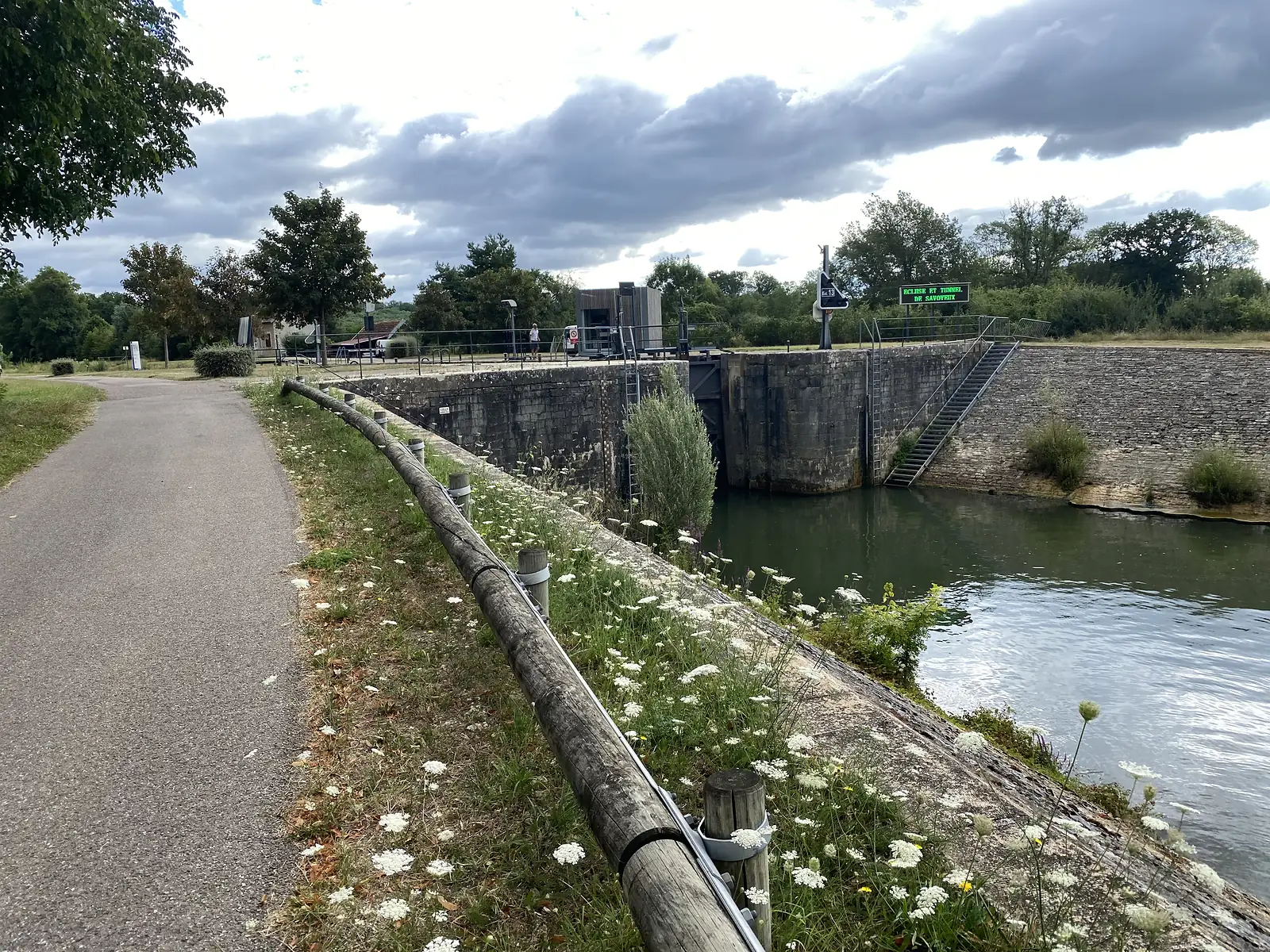 A stone canal lock with a signpost reading "Ecluse et Tunnel de Savoyeux", steps leading down to the dark green water.