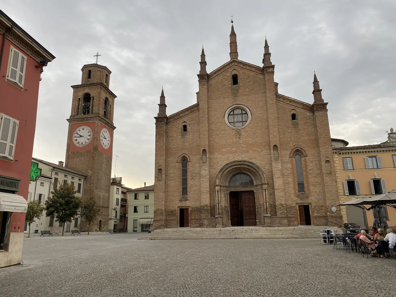 The twin-towered brick facade of Fidenza Cathedral with its ornate rose window, seen across an empty piazza at dusk.