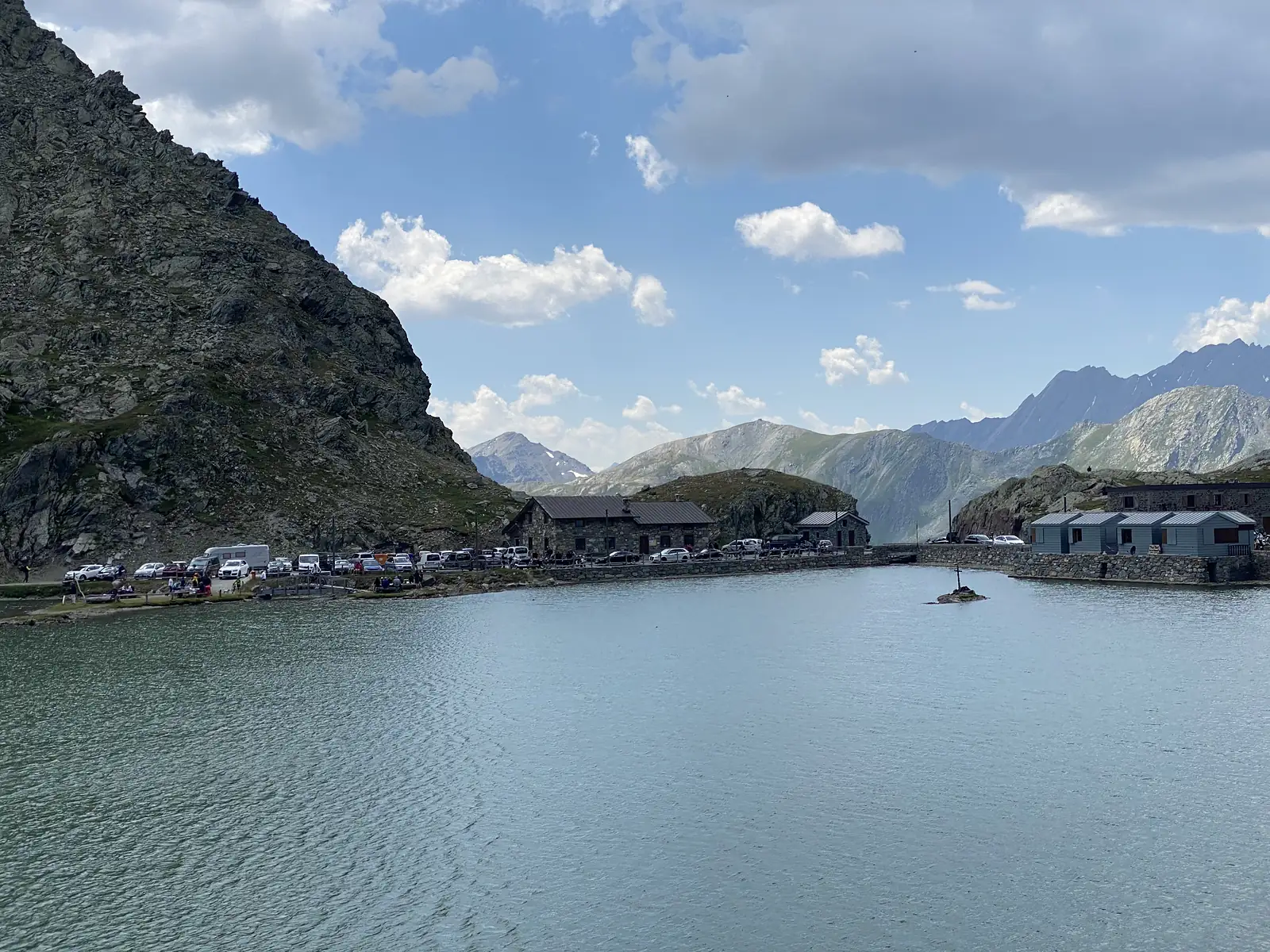 
The pass lake under a heavily clouded sky, with stone and timber buildings and parked cars lining its near shore.
