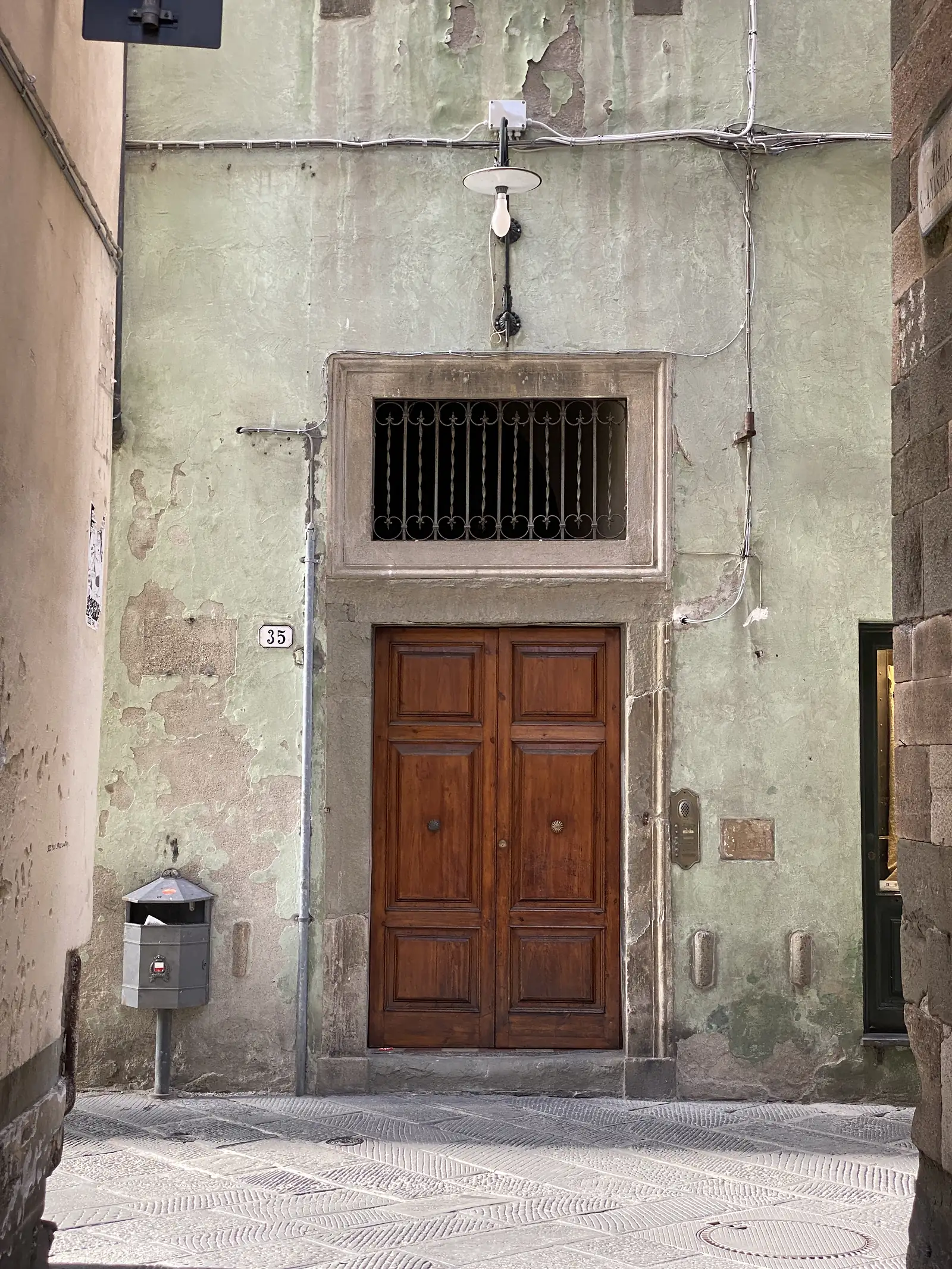 A panelled wooden front door beside a barred window on a pale green rendered house wall, with the number "35" on a small plaque below.