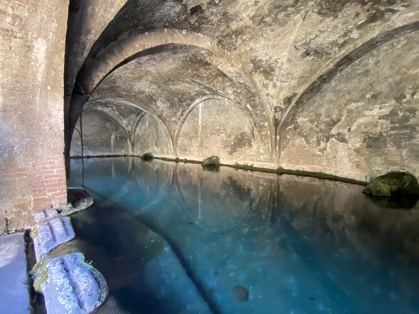 A cross-vaulted brick cistern filled with still turquoise water, its arches reflected in the surface.
