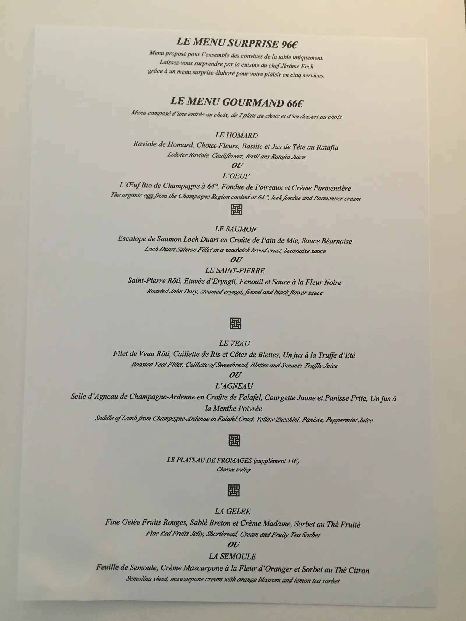 A restaurant tasting menu headed 'Le Menu Surprise 96€' and 'Le Menu Gourmand 66€', listing courses such as lobster raviole, John Dory and saddle of Champagne-Ardenne lamb in French with English translations.
