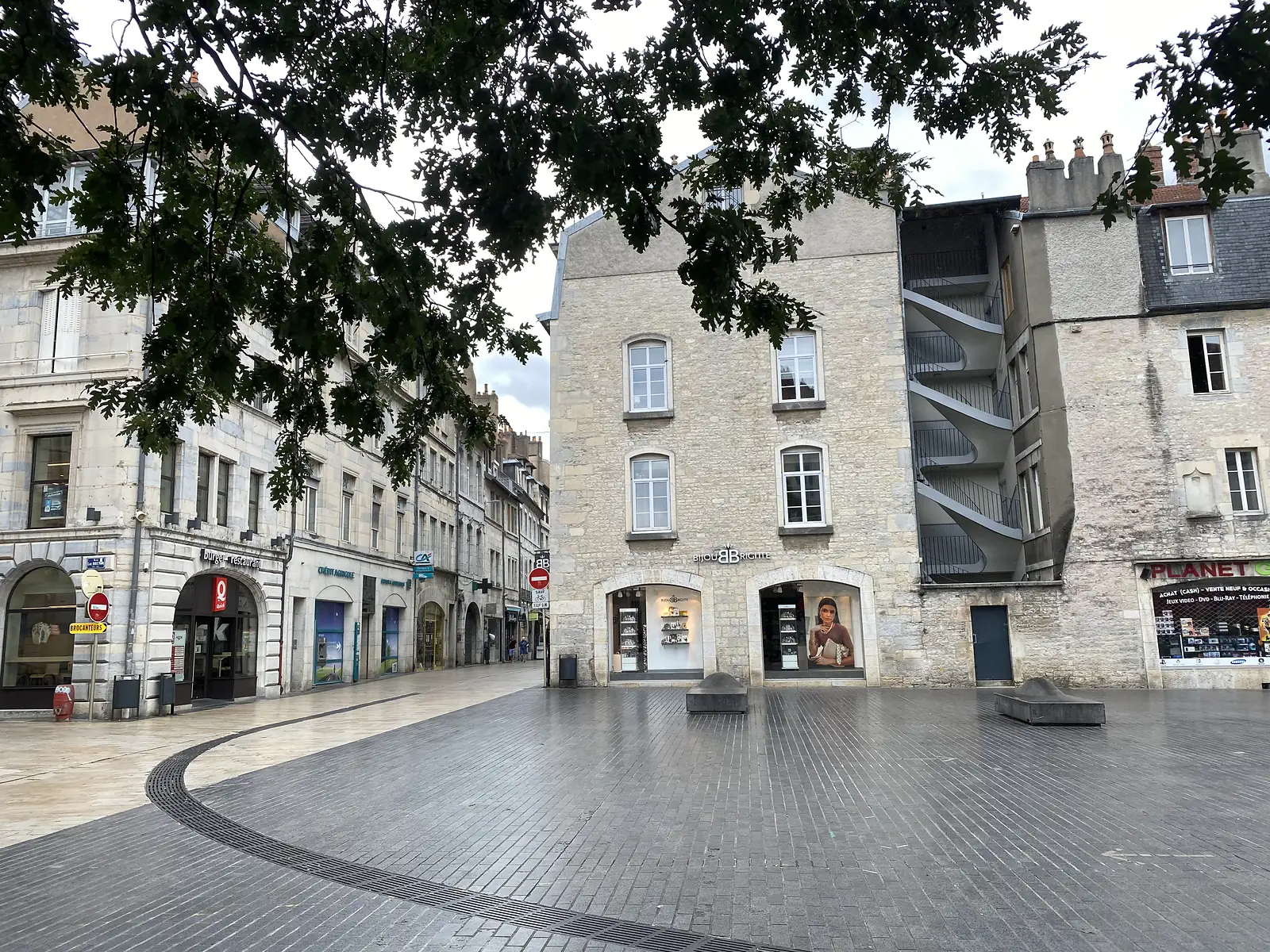 A stone-built corner house with a spiral external staircase and jewellery shop stands on a quiet paved square in Besançon's old town.