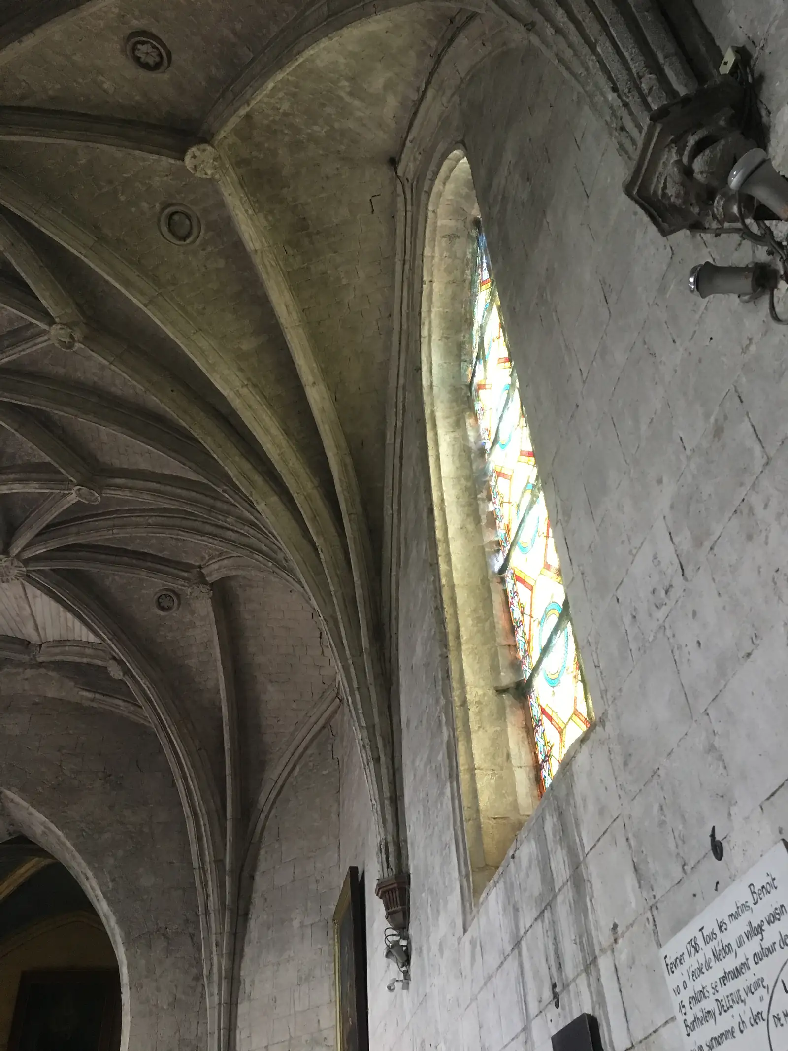 A stone church ceiling curves up to a rectangular stained-glass skylight glowing above ribbed vaulting.