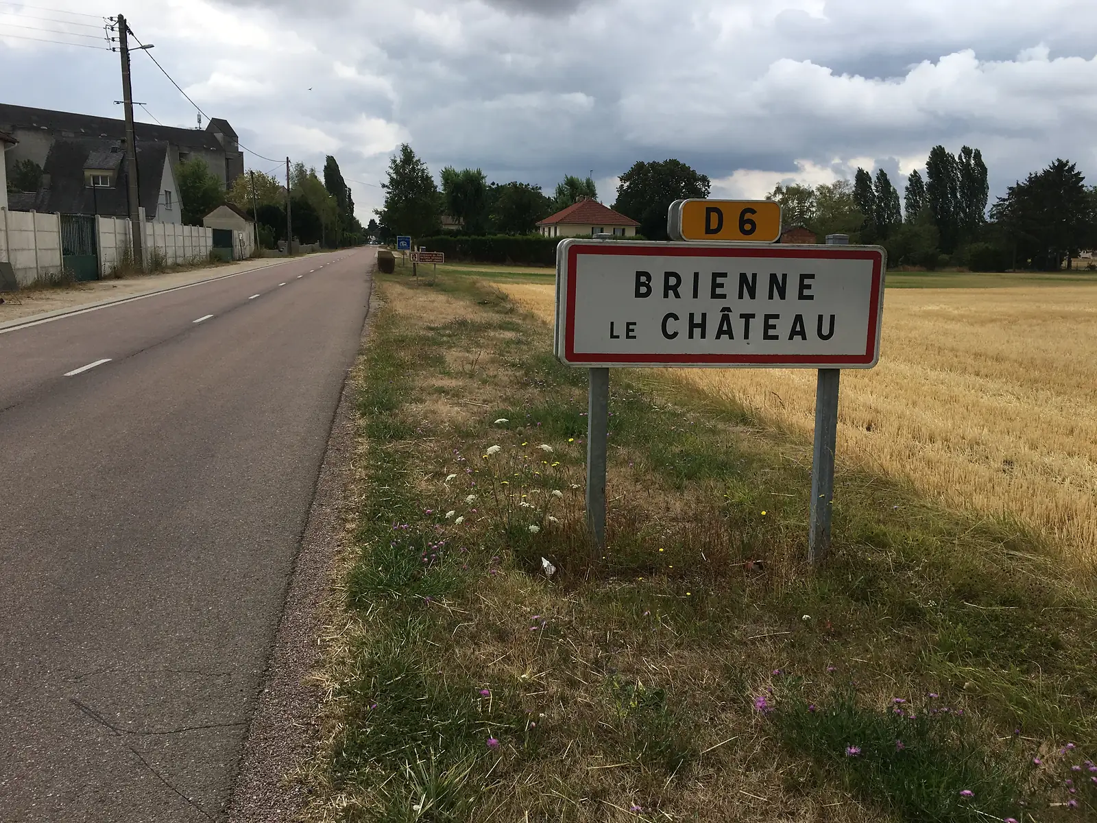 A road sign marking the entrance to Brienne-le-Château on the D6, standing in grass beside a field of stubble.